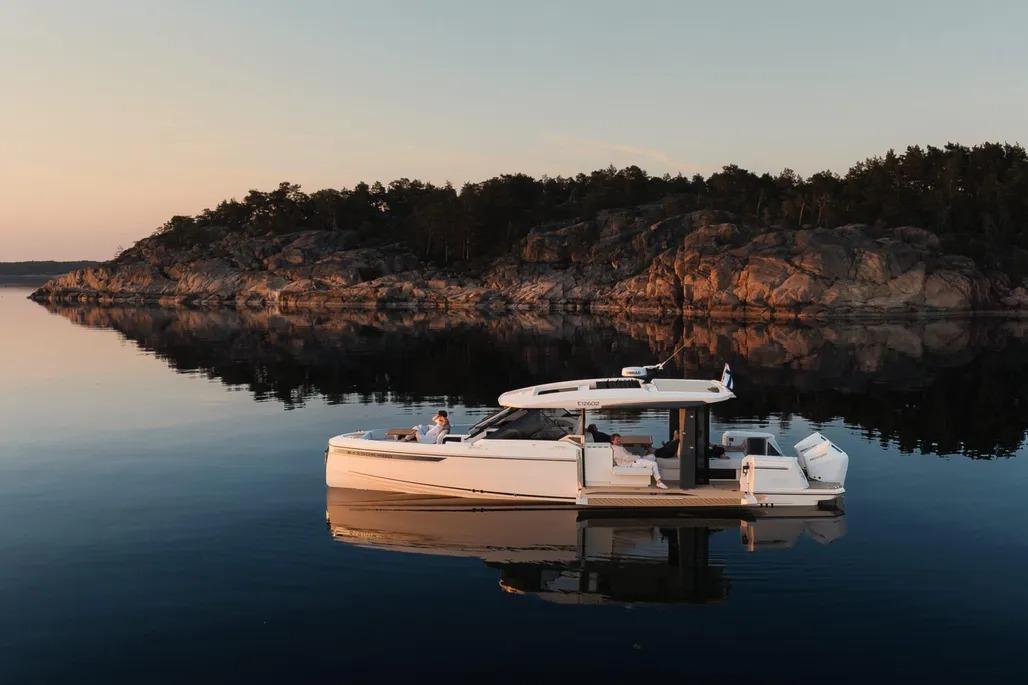 2025 Saxdor 400 GTO yacht on serene water, rocky shoreline backdrop at sunset.