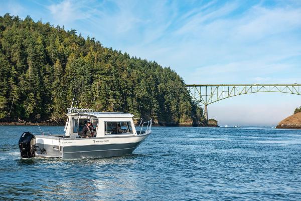 2023 Spartan 220 Maximus Pro boat cruising near a scenic bridge and forested shoreline.