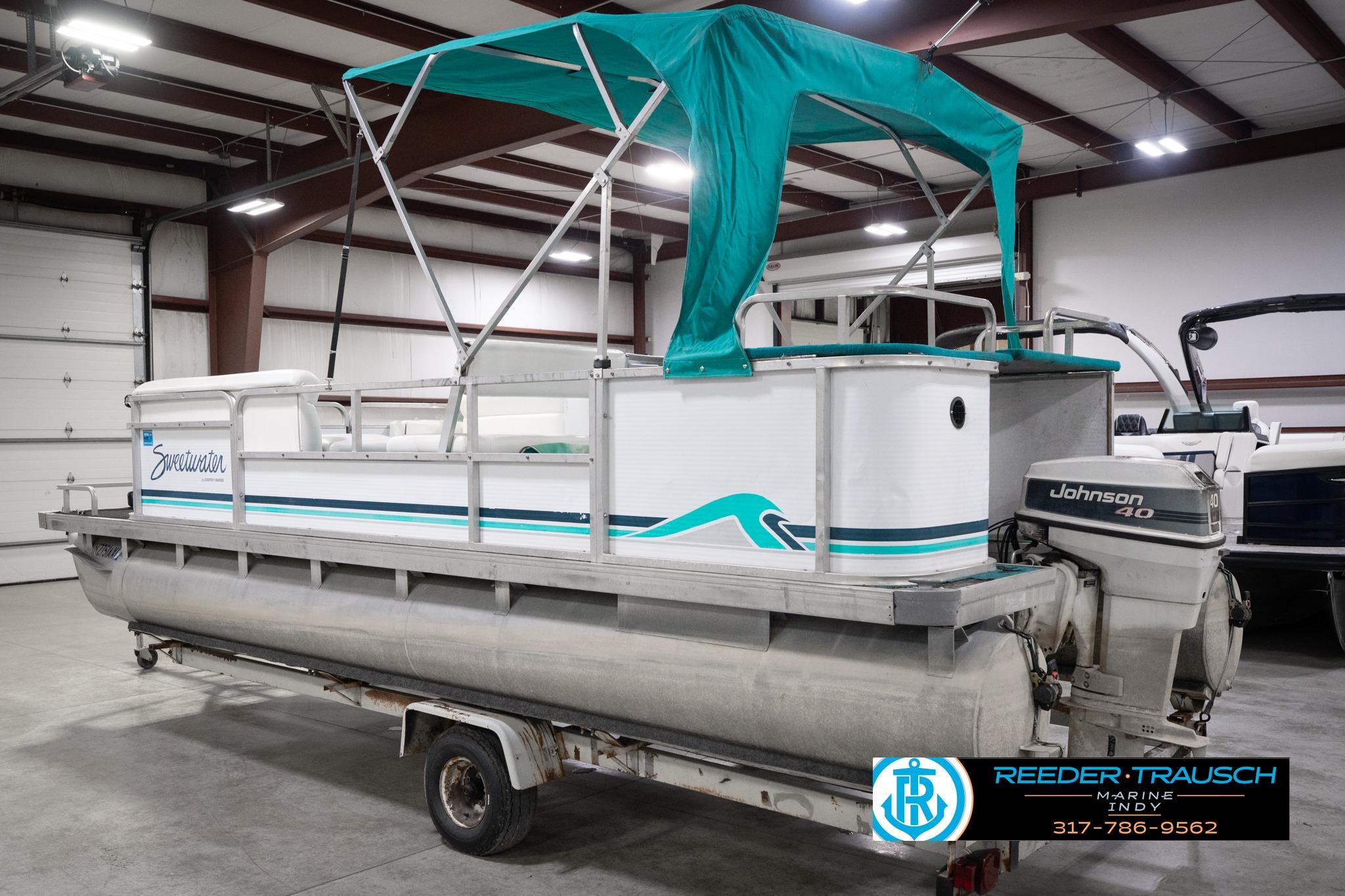 1992 Godfrey Sweetwater pontoon boat with teal canopy and Johnson 40 engine in a warehouse.