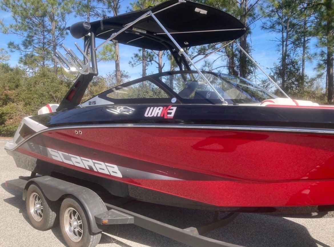 A red 2017 Scarab 215 boat on a trailer, surrounded by trees.