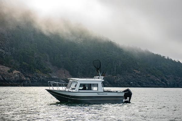 2023 Spartan 220 Maximus Pro boat cruising near a misty forested shoreline.