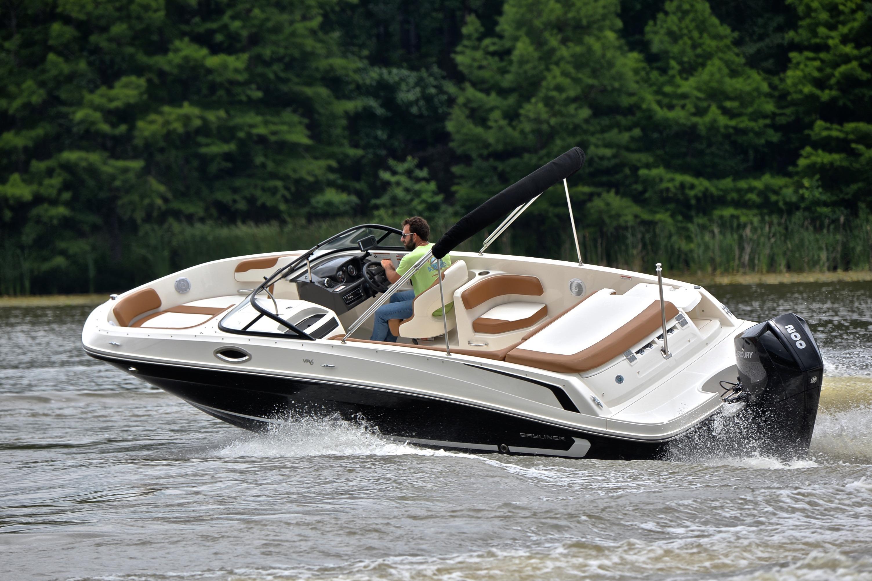 2019 Bayliner VR6 Bowrider OB cruising on a lake with lush green trees.