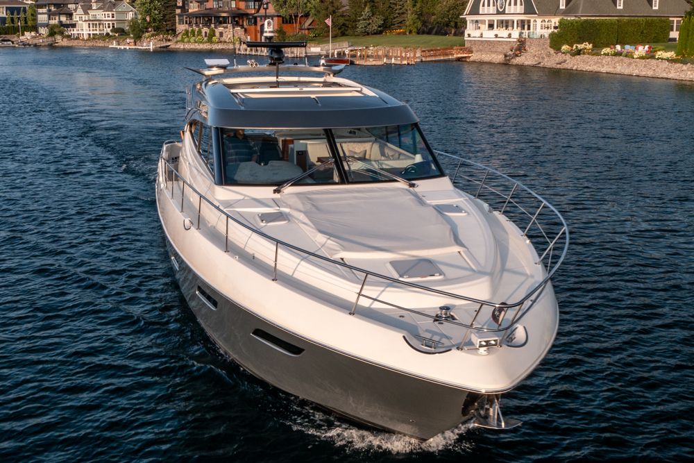 2022 Riviera 6000 Sport Yacht Platinum cruising on a serene lake near luxury homes.