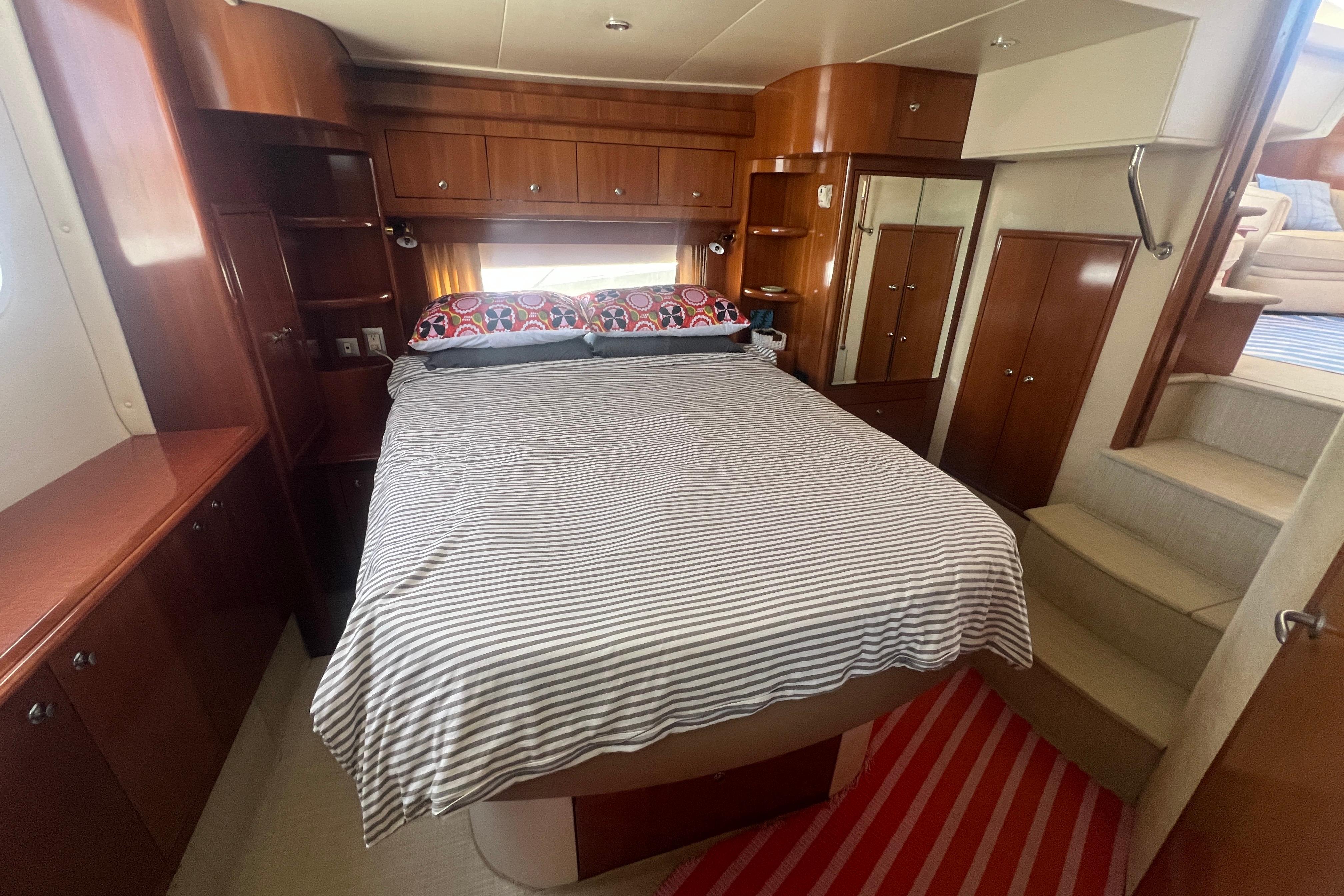 Interior of 2006 Carver 43 Motor Yacht bedroom with striped bedding and wooden cabinetry.