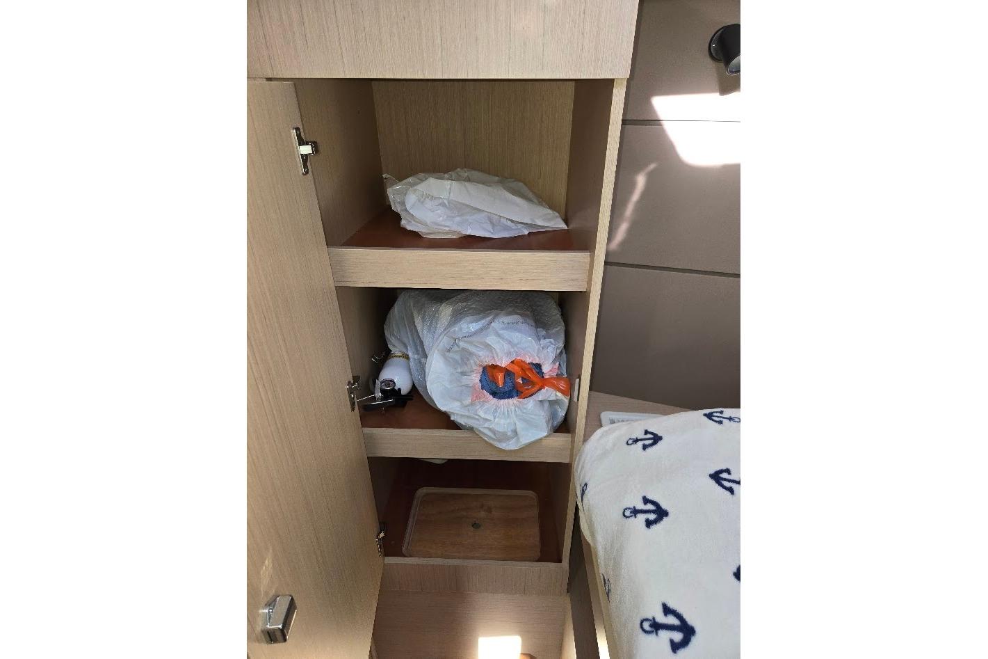 Cabinet storage inside 2023 Beneteau Oceanis 38.1 yacht with shelves and nautical-themed bedding.