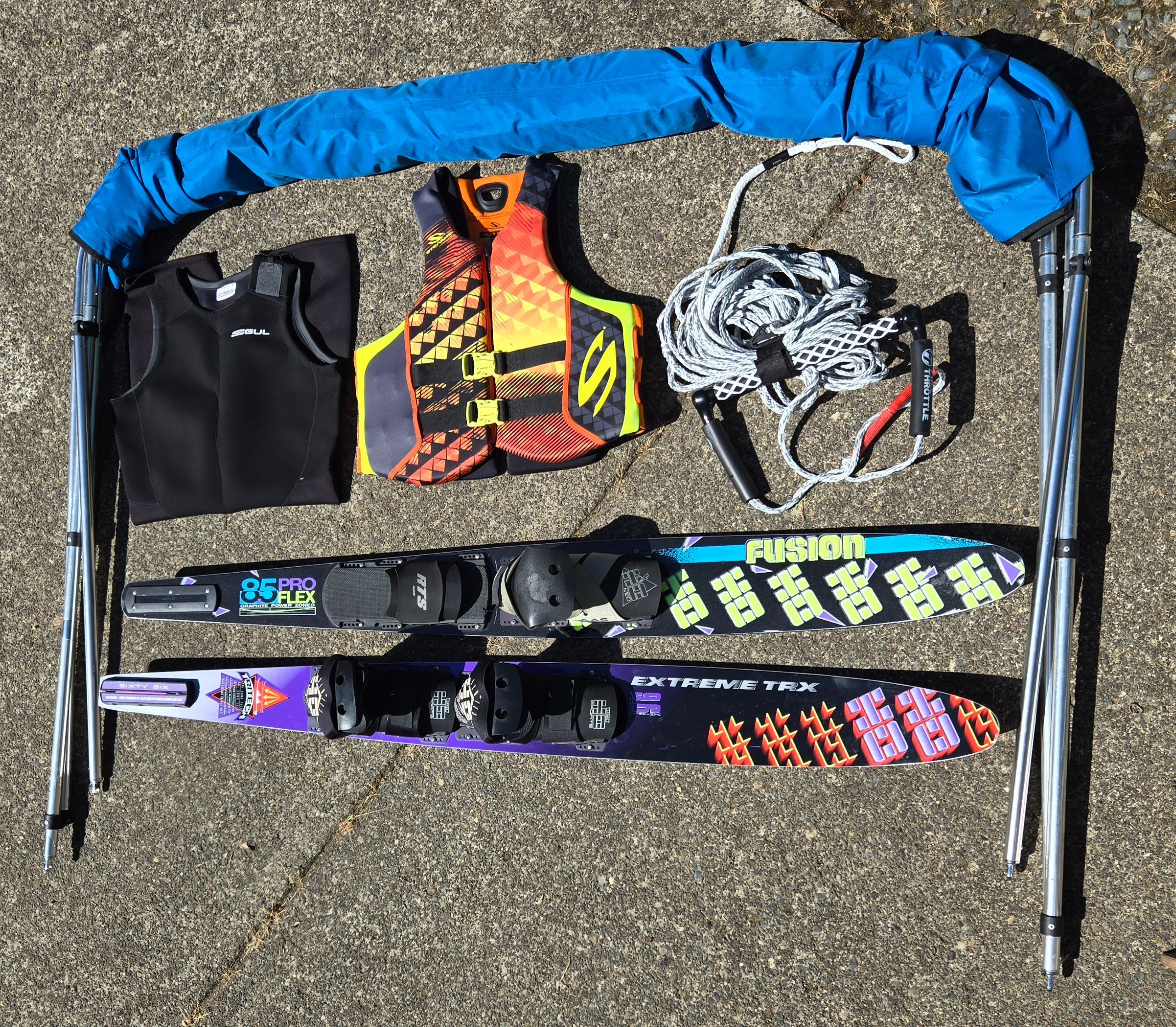 Water skiing gear with life jacket, rope, and skis on concrete ground.