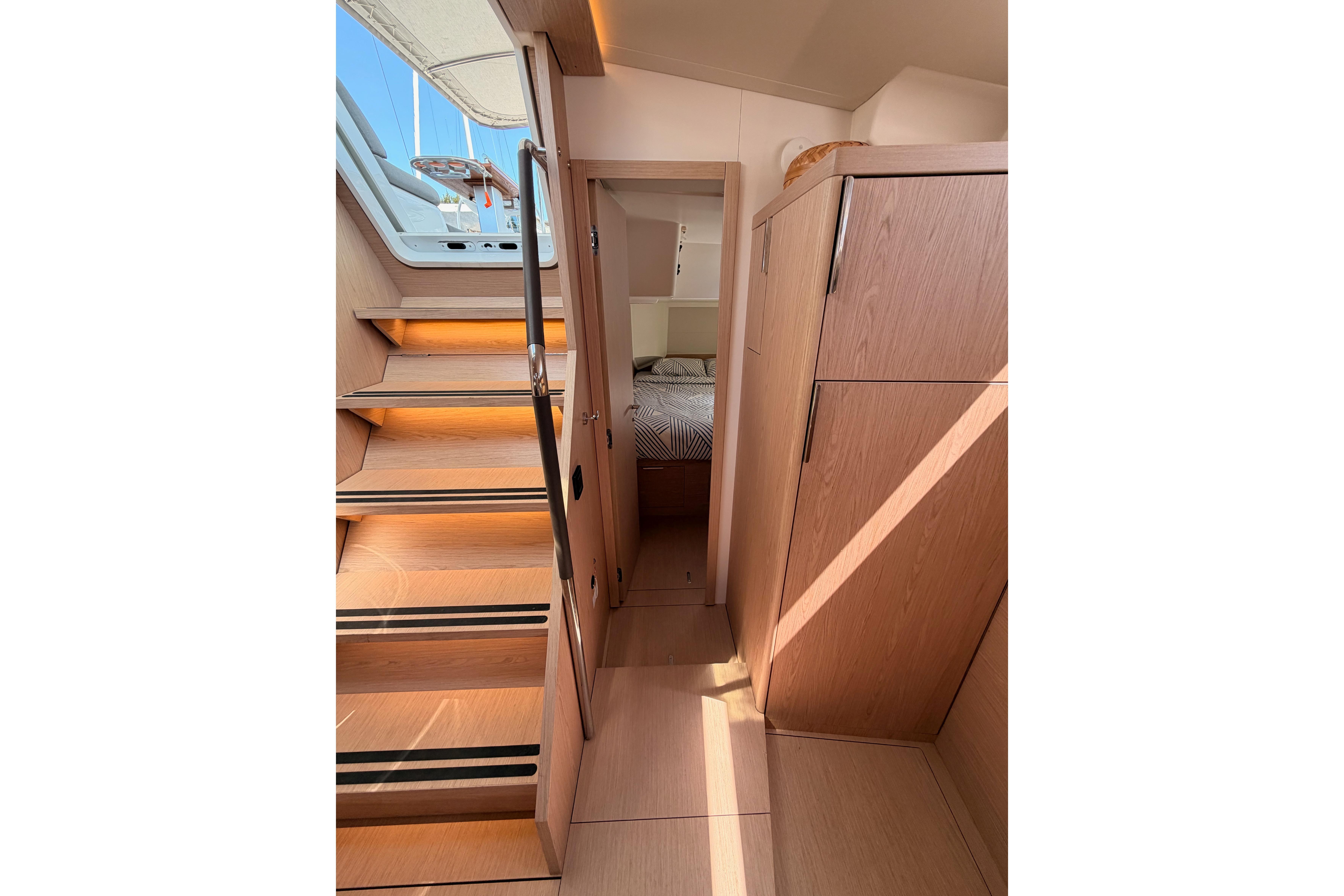Interior of 2022 Beneteau Oceanis Yacht 54, featuring wooden stairs and cabin entrance.