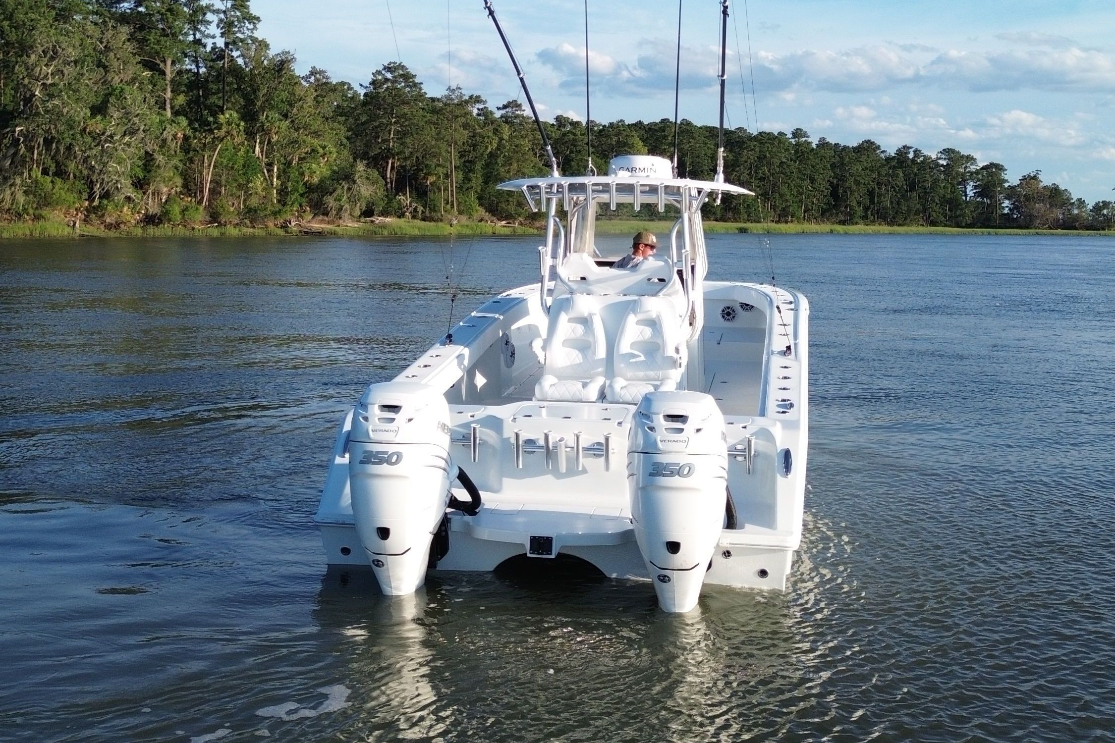 A white boat cruising on a calm river, surrounded by trees.