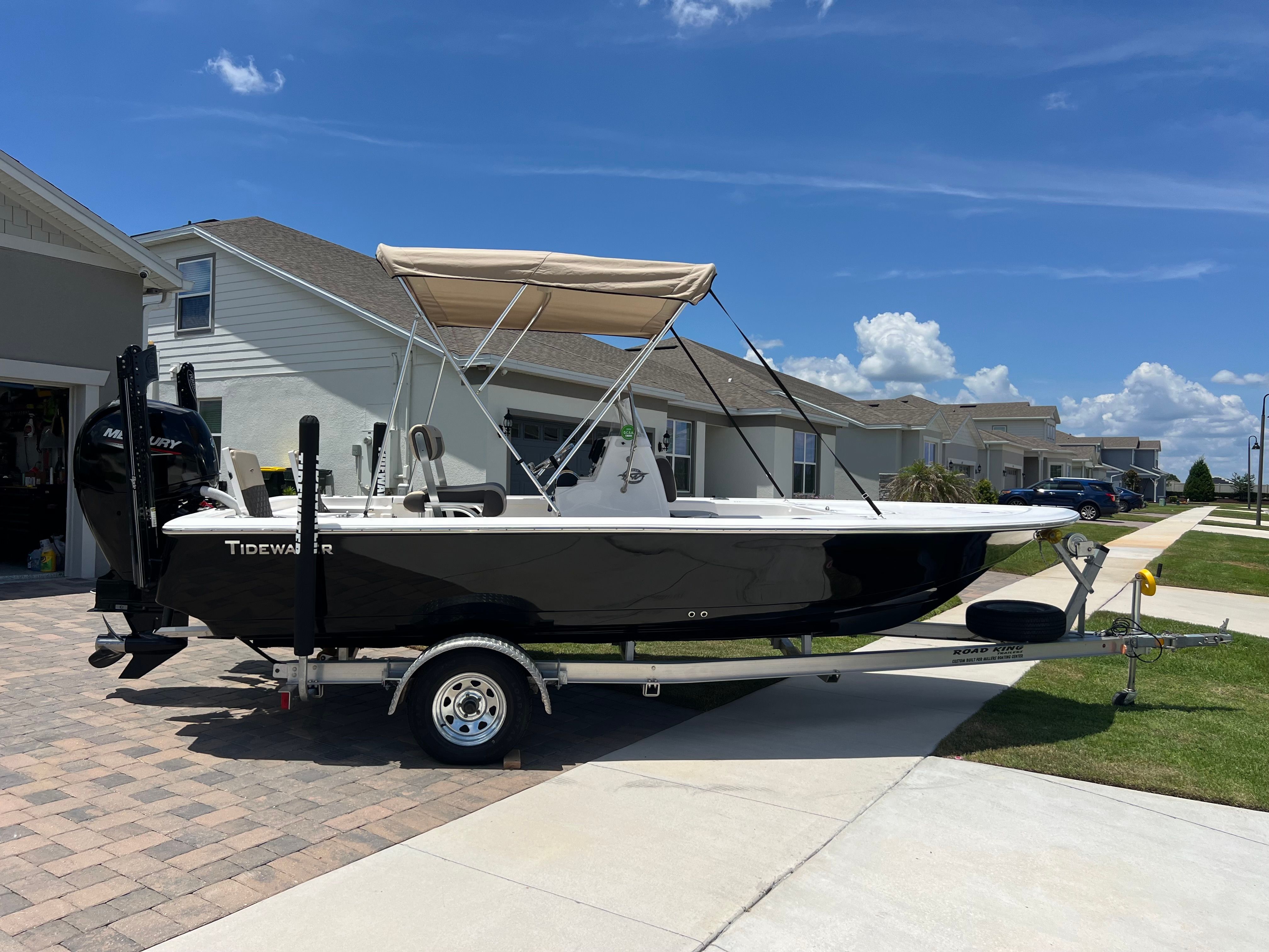 A black 2021 Tidewater 1910 Bay Max boat on a trailer in a residential area.