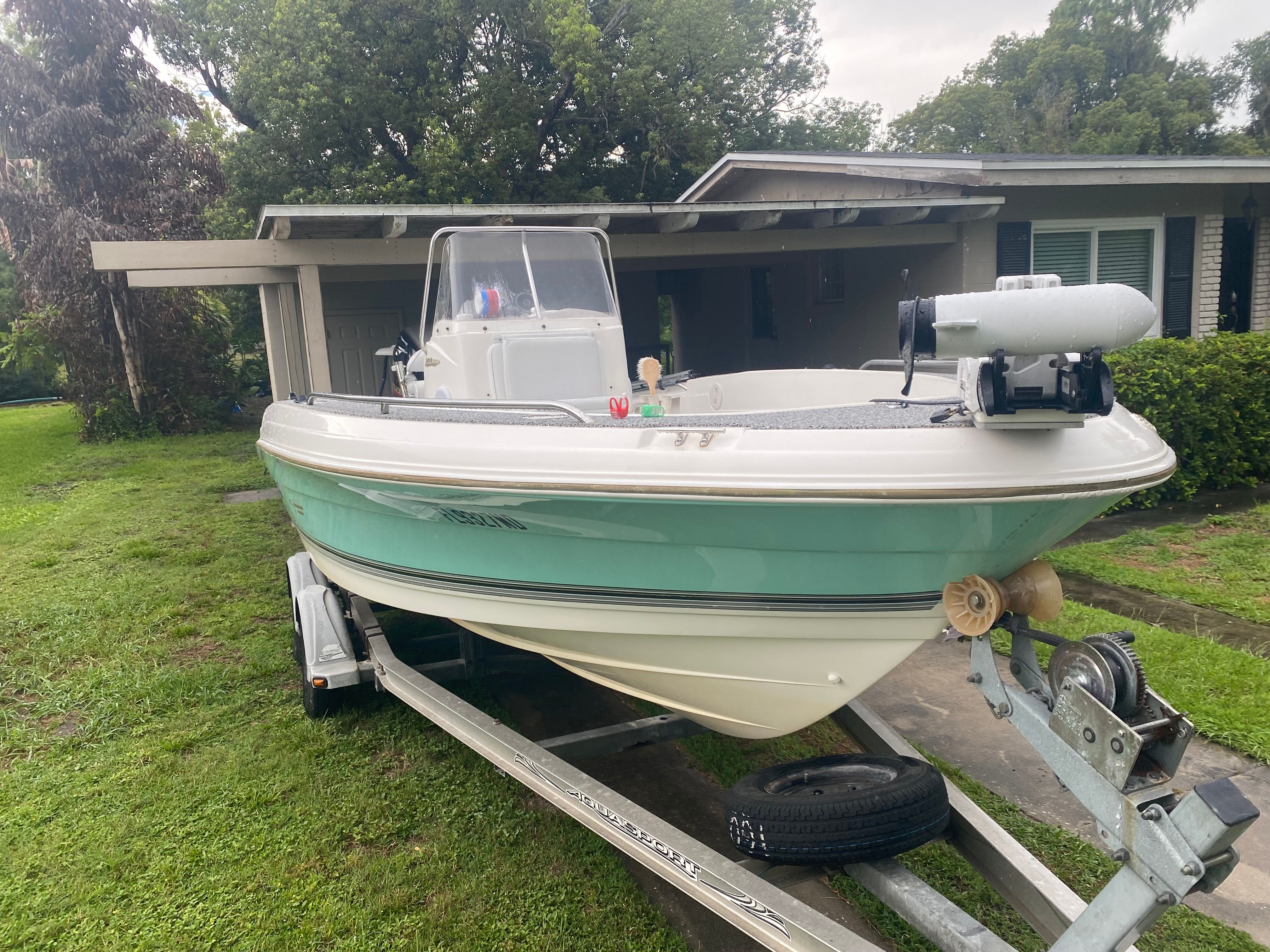 A 2003 Aquasport 201 Osprey boat on a trailer in front of a house.