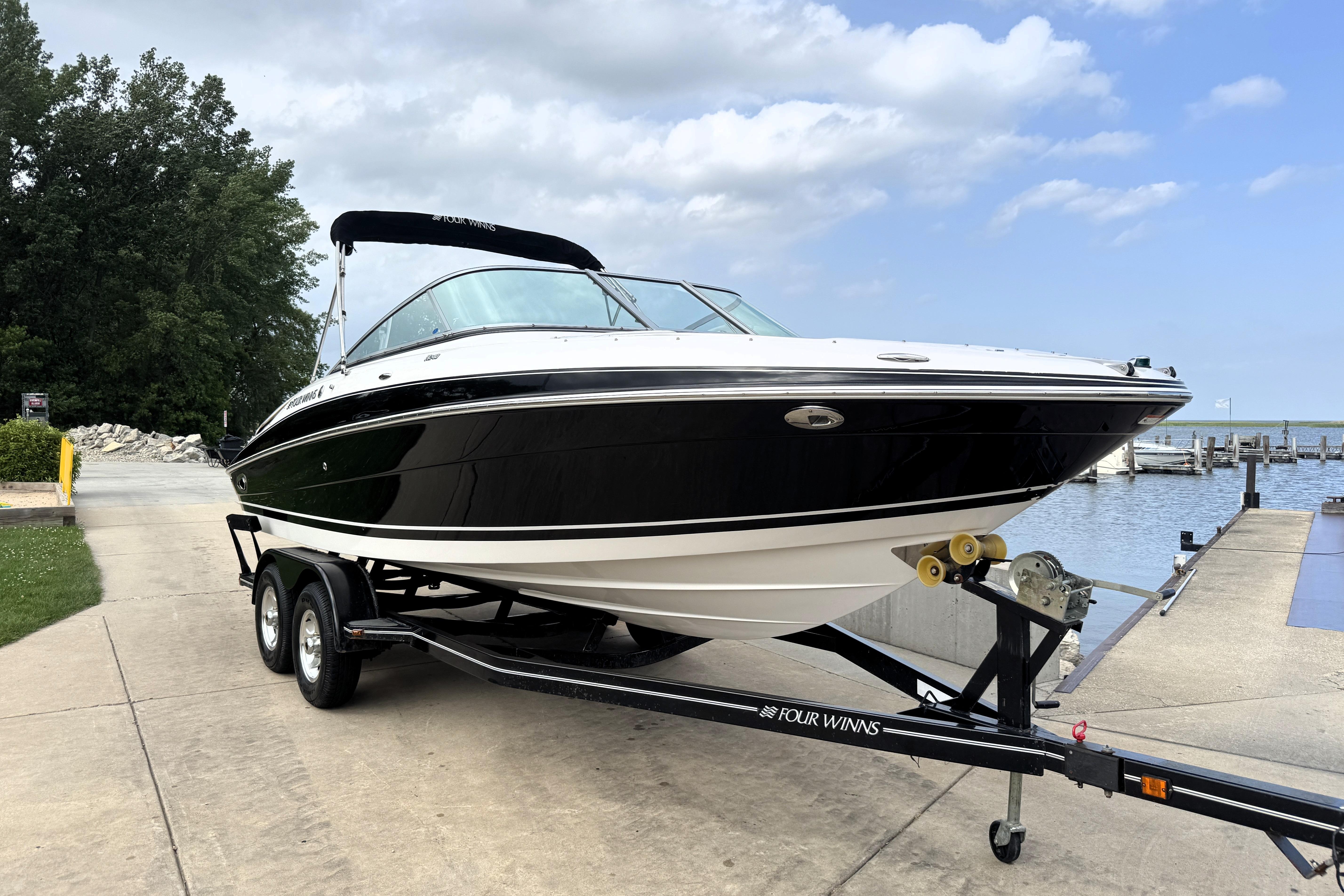 2008 Four Winns H240 boat on trailer near a dock, under a partly cloudy sky.