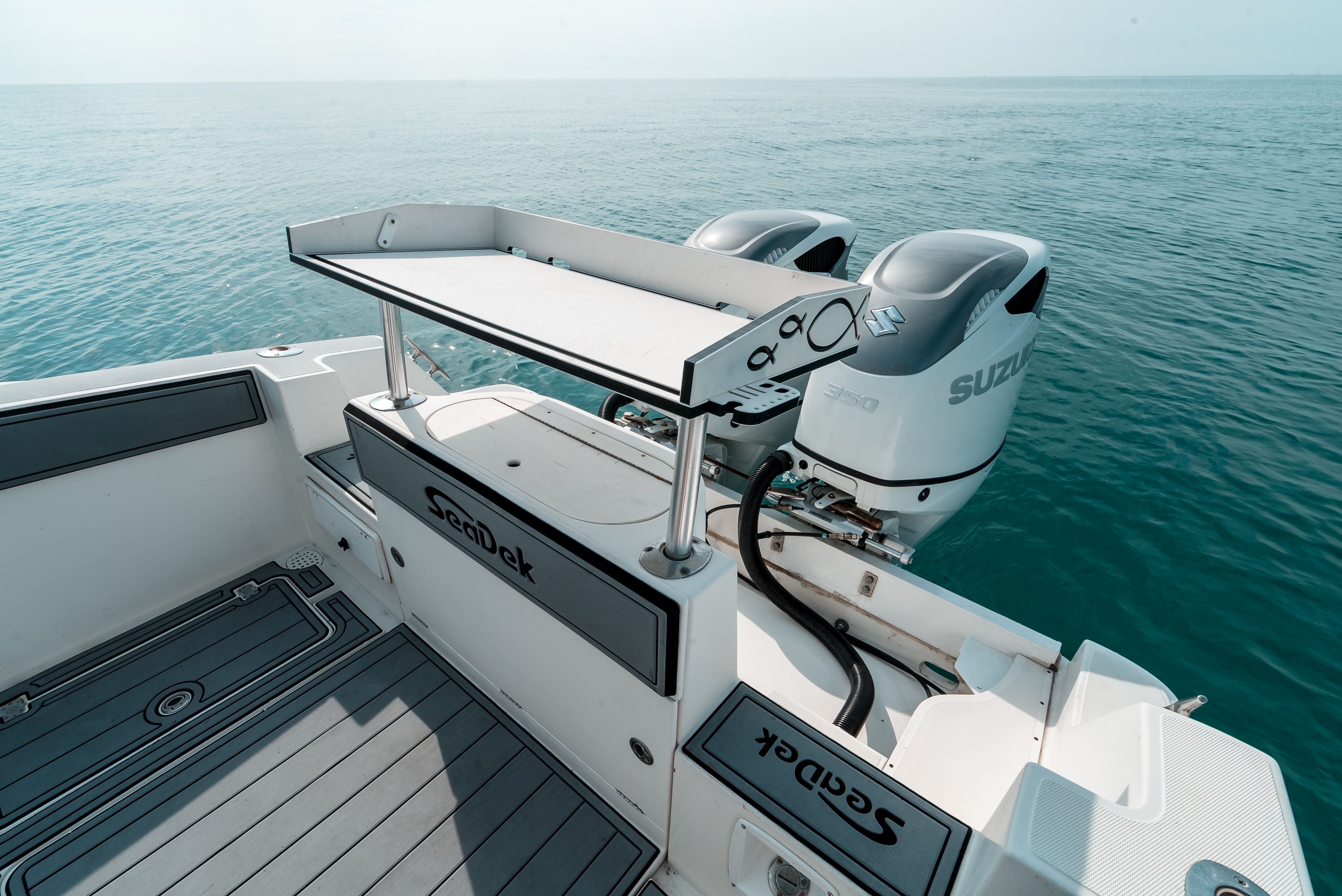 The image shows the stern of a boat with two Suzuki outboard motors on calm water.