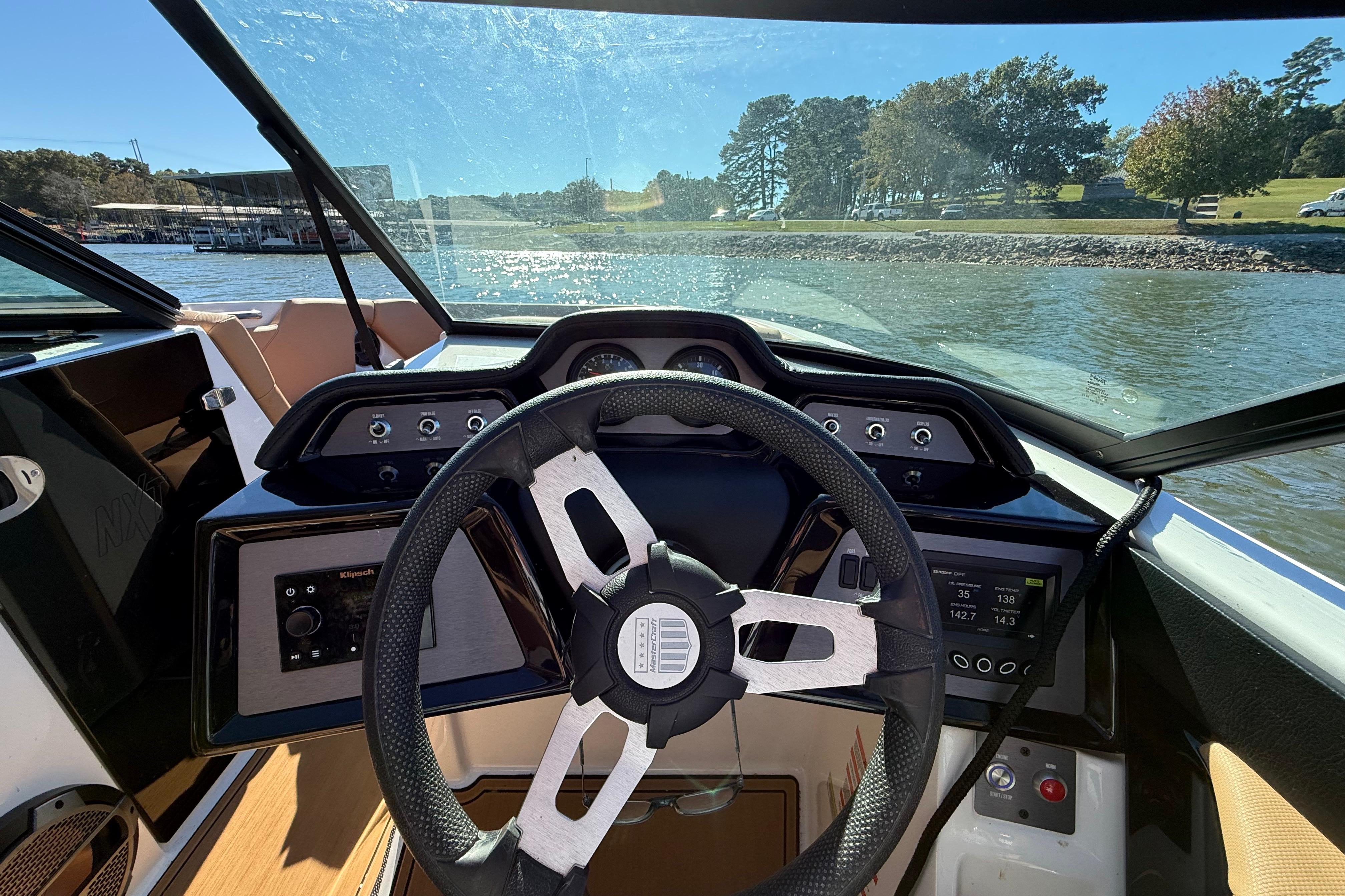 2022 MasterCraft NXT24 boat dashboard with steering wheel, on a sunny day by the lake.