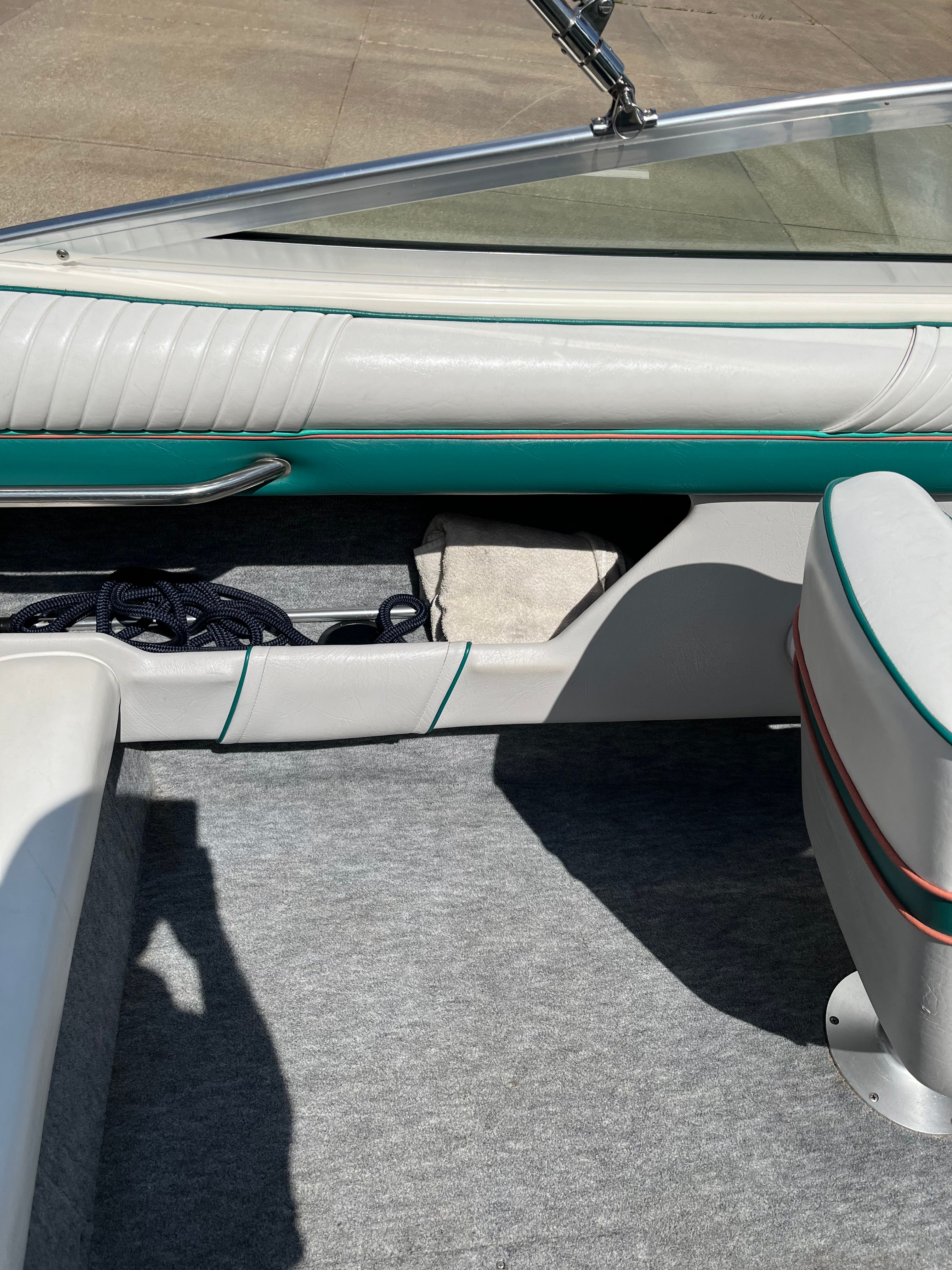 Interior view of a boat with white and green seats and gray carpet flooring.