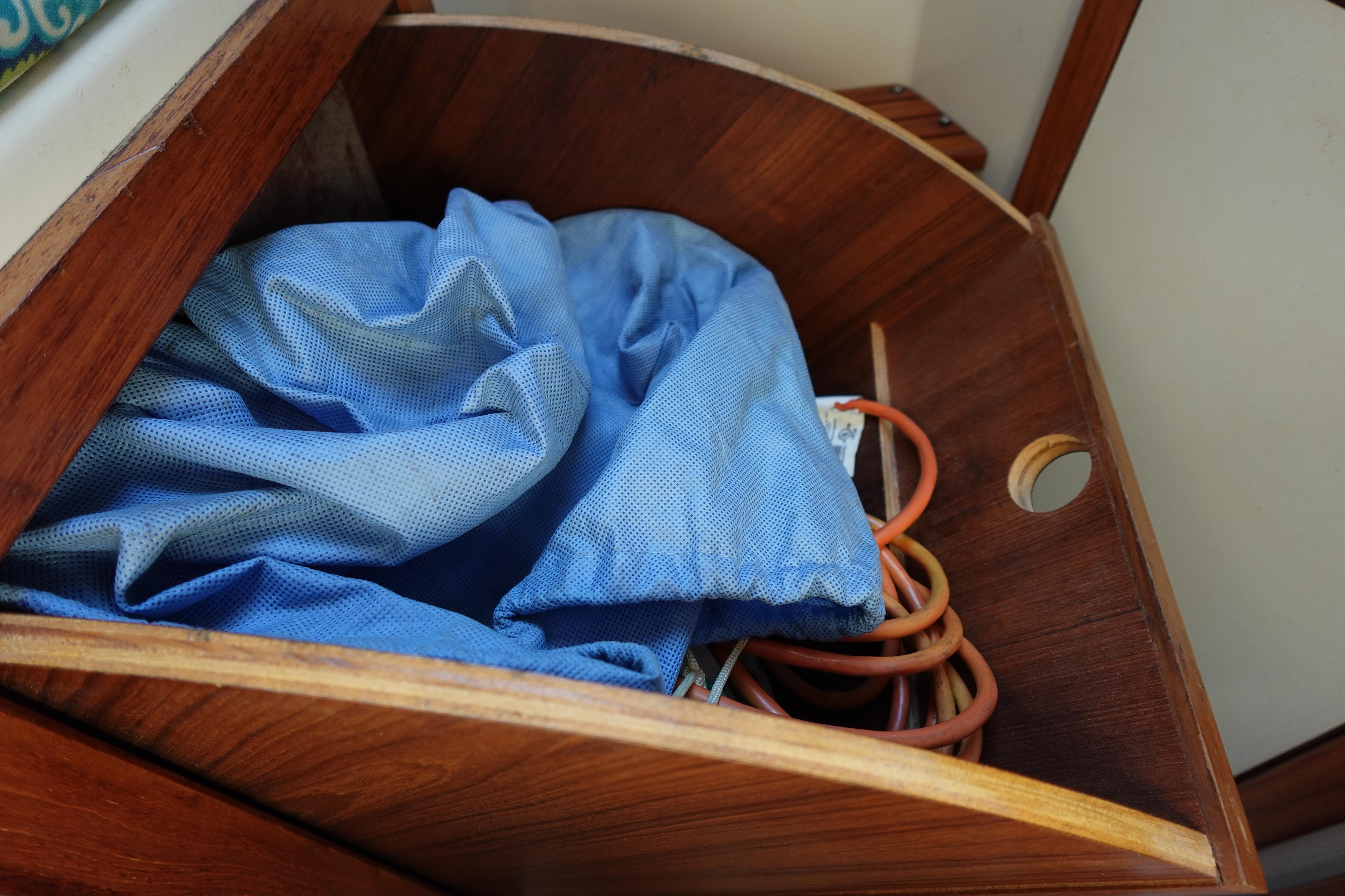 Wooden storage compartment in a 1997 Catalina 28 sailboat with blue fabric and cables.
