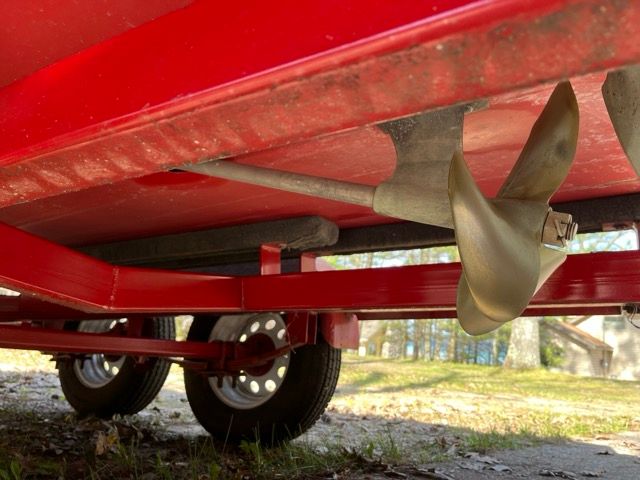 Close-up of a boat propeller and trailer, surrounded by trees.