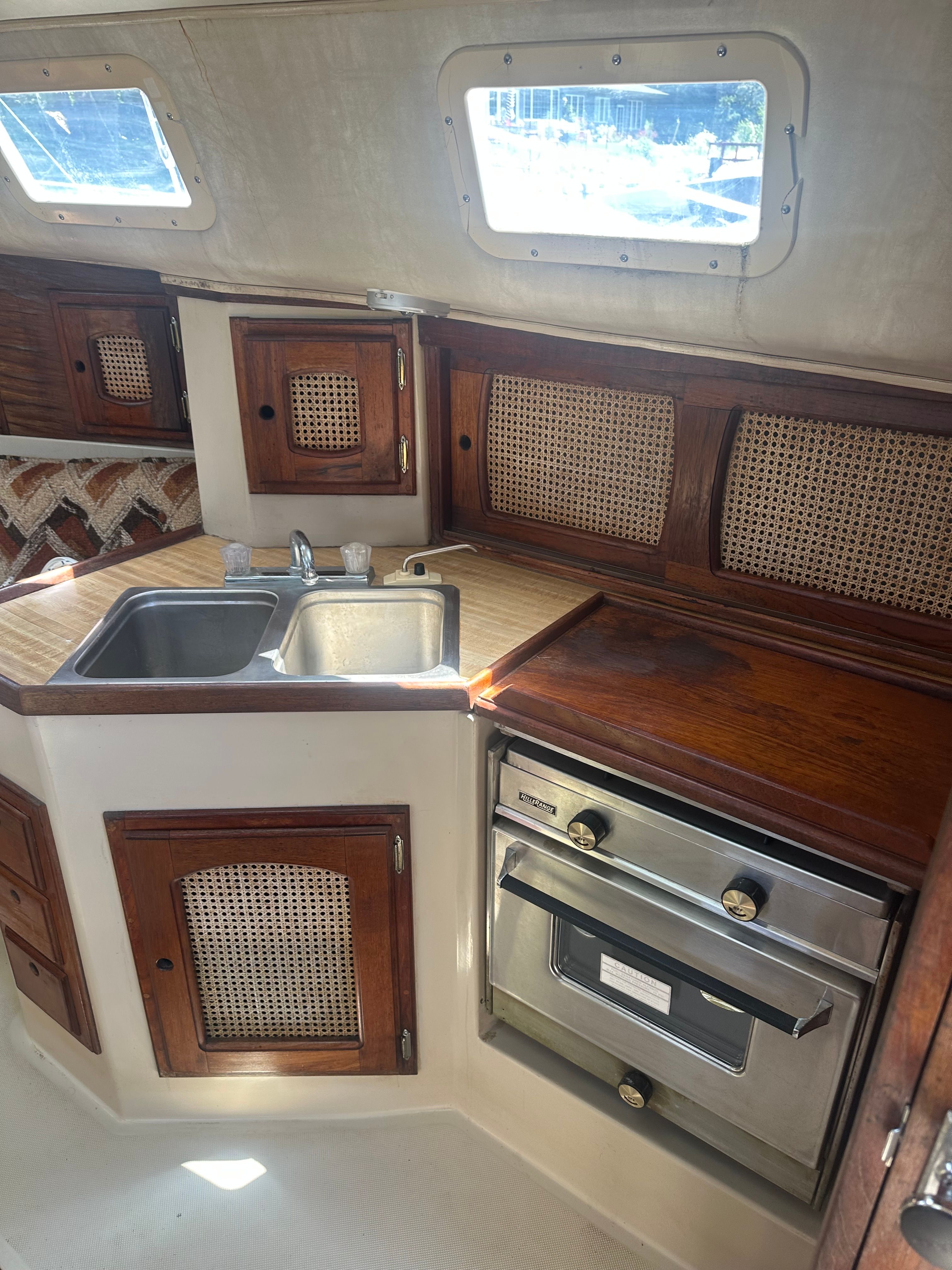 The galley of a 1982 Lancer 30 yacht with a sink, stove, and wooden cabinets.