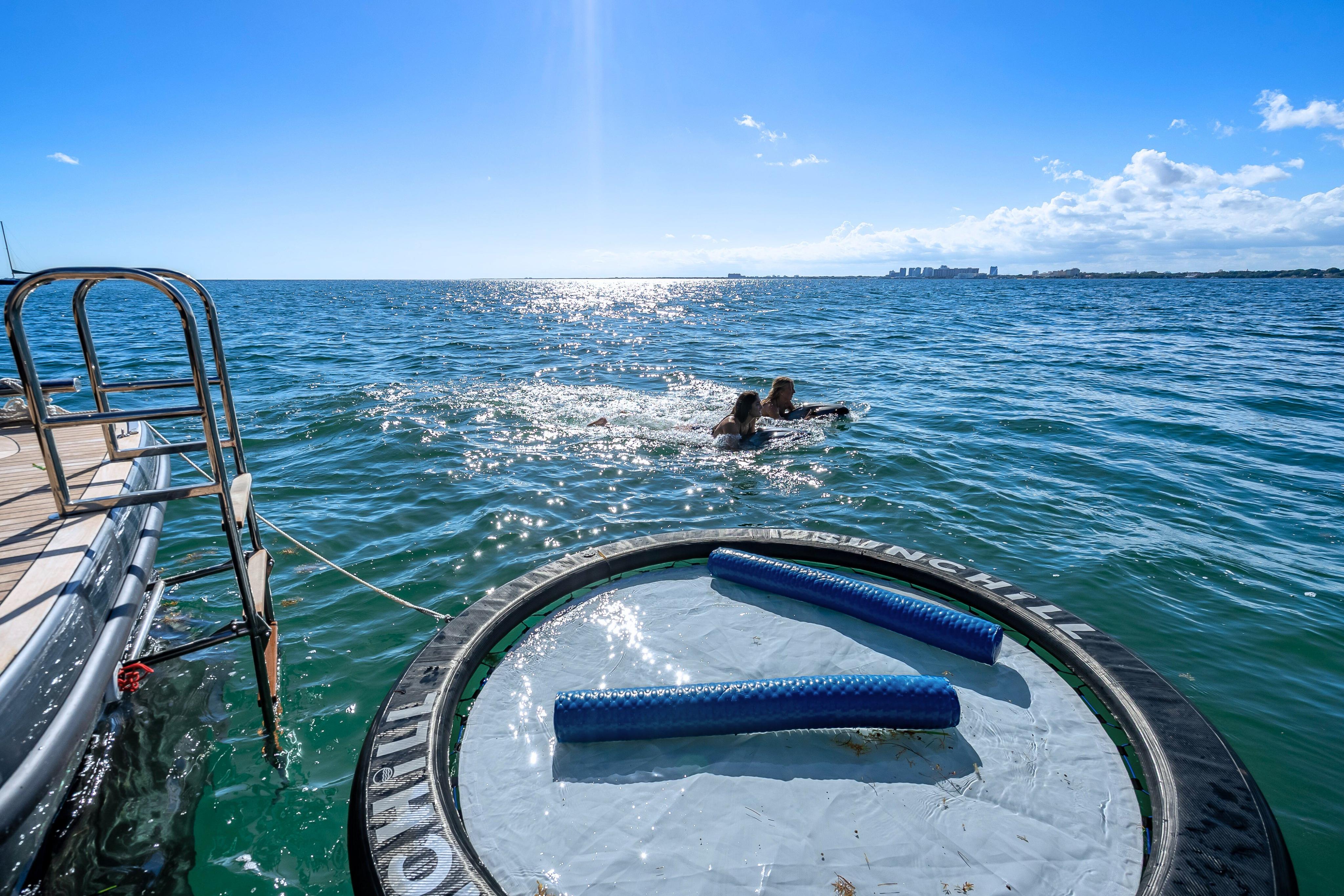 Sunreef 60 Power yacht with swimmers and floating mat on sunny ocean, 2026 model.