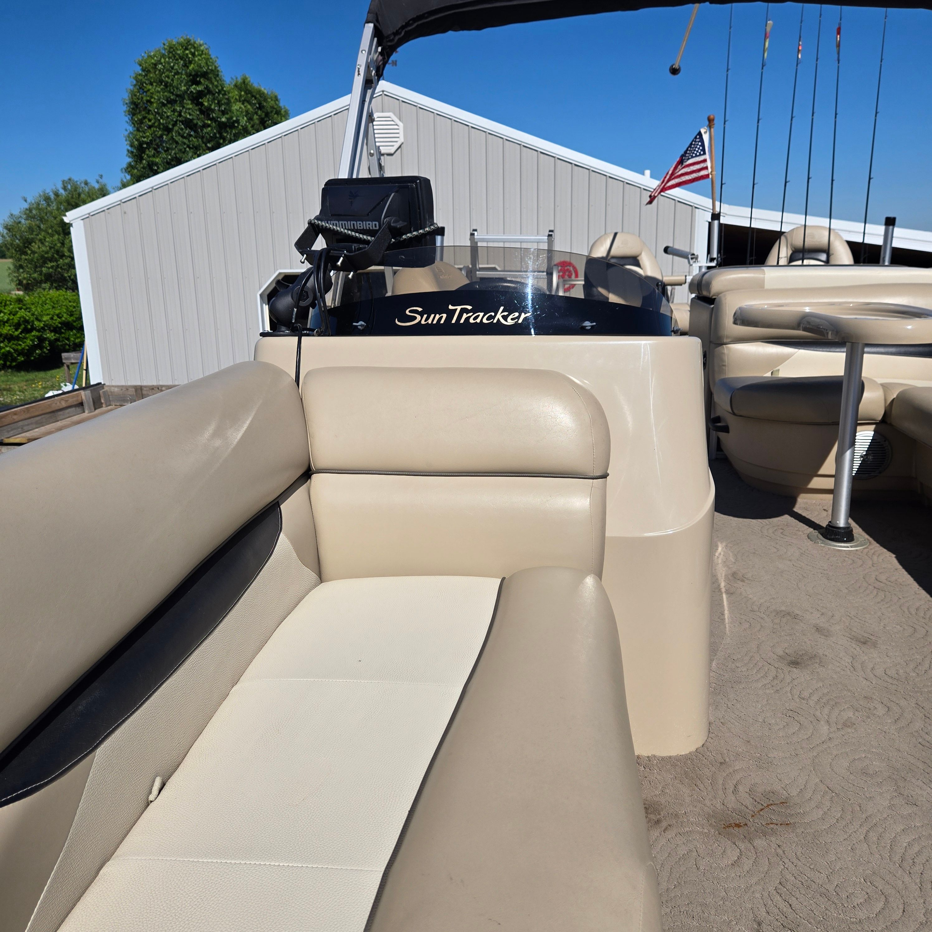 The image shows the deck of a 2012 Sun Tracker Fishin' Barge 24 DLX with beige seating.