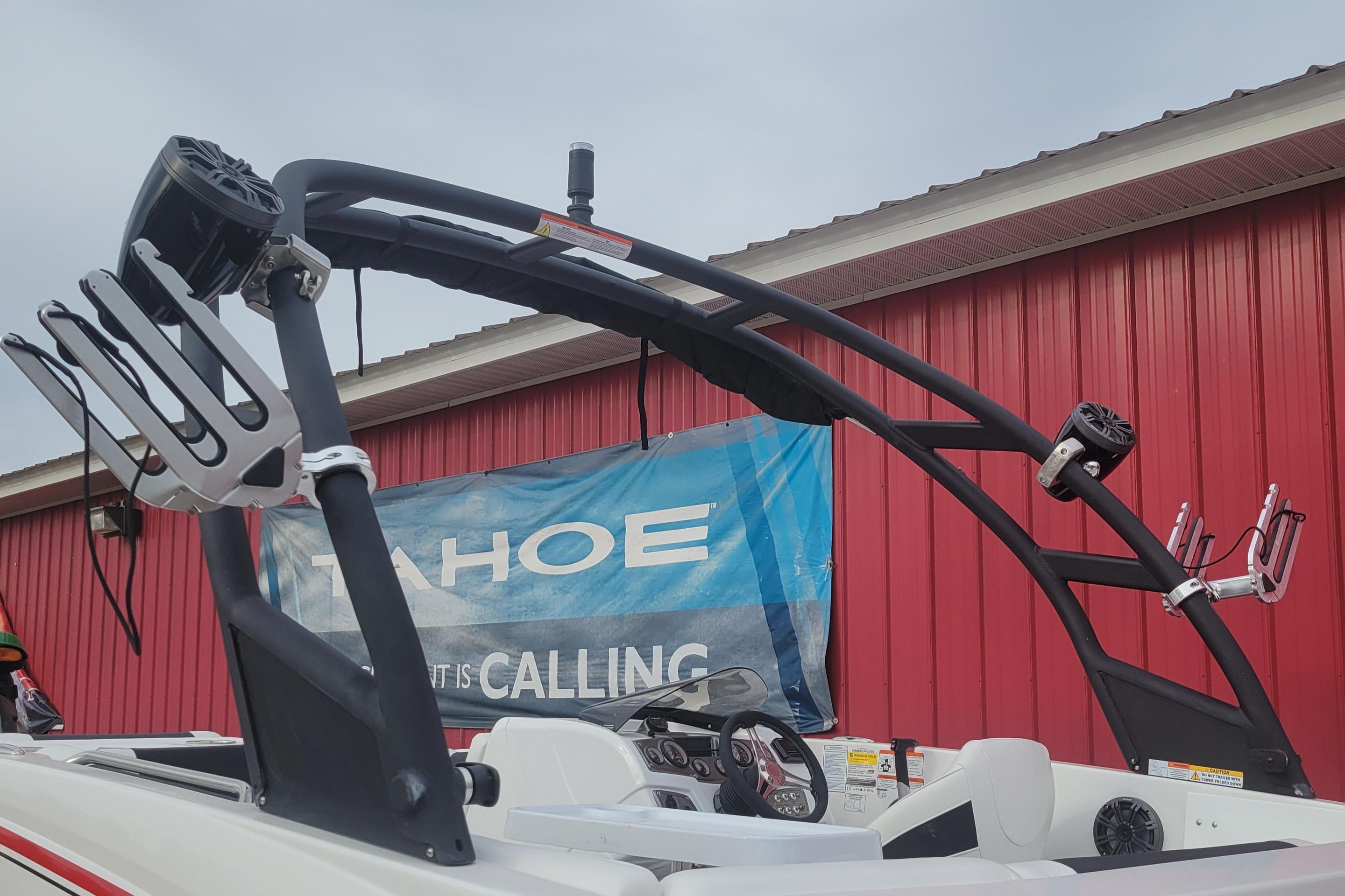 Tahoe 1950 boat, 2023 model, with wakeboard tower and speakers, against red building.