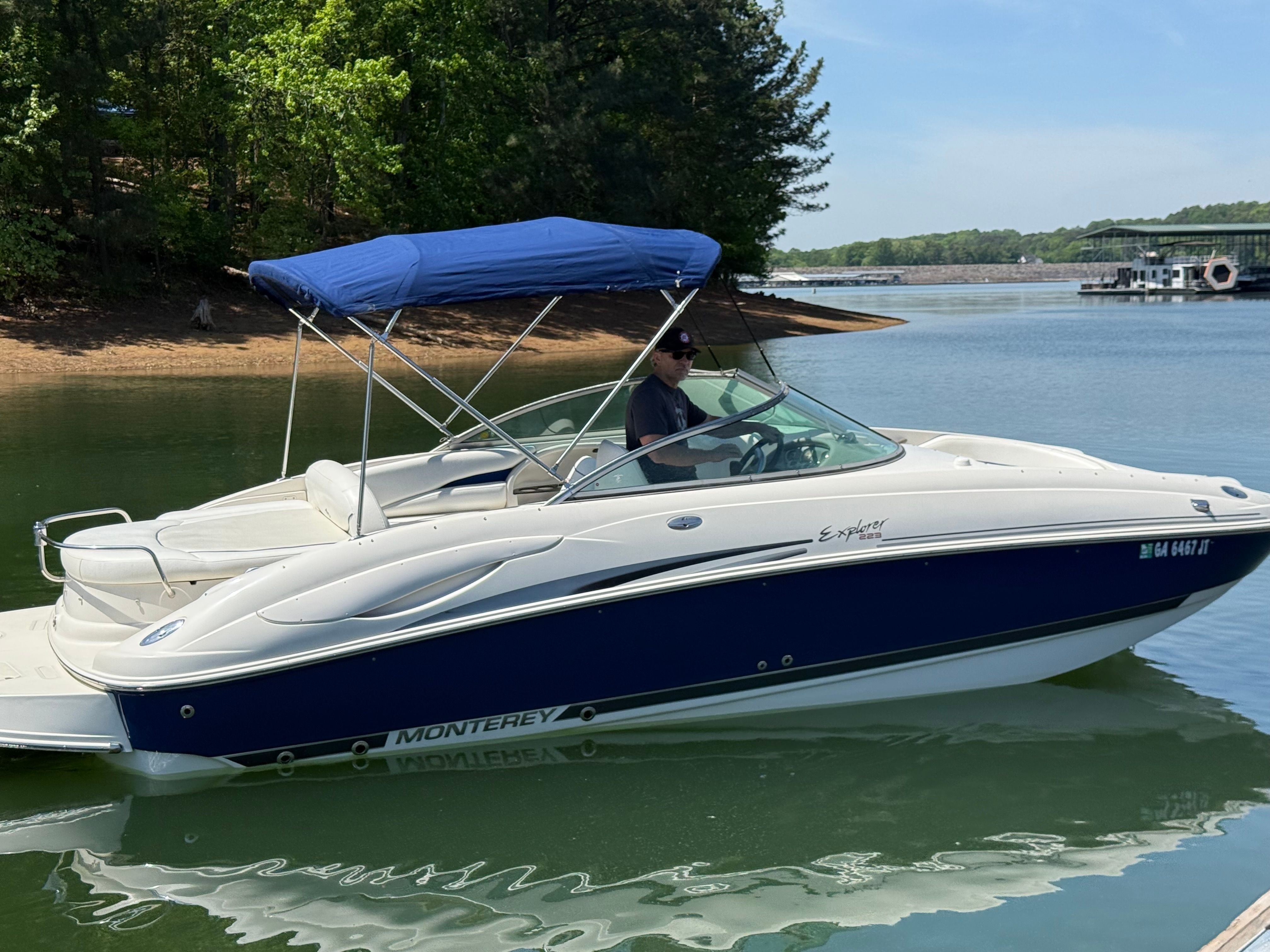 A 2005 Monterey 223 Explorer Sport on a calm lake, featuring a blue sunshade.