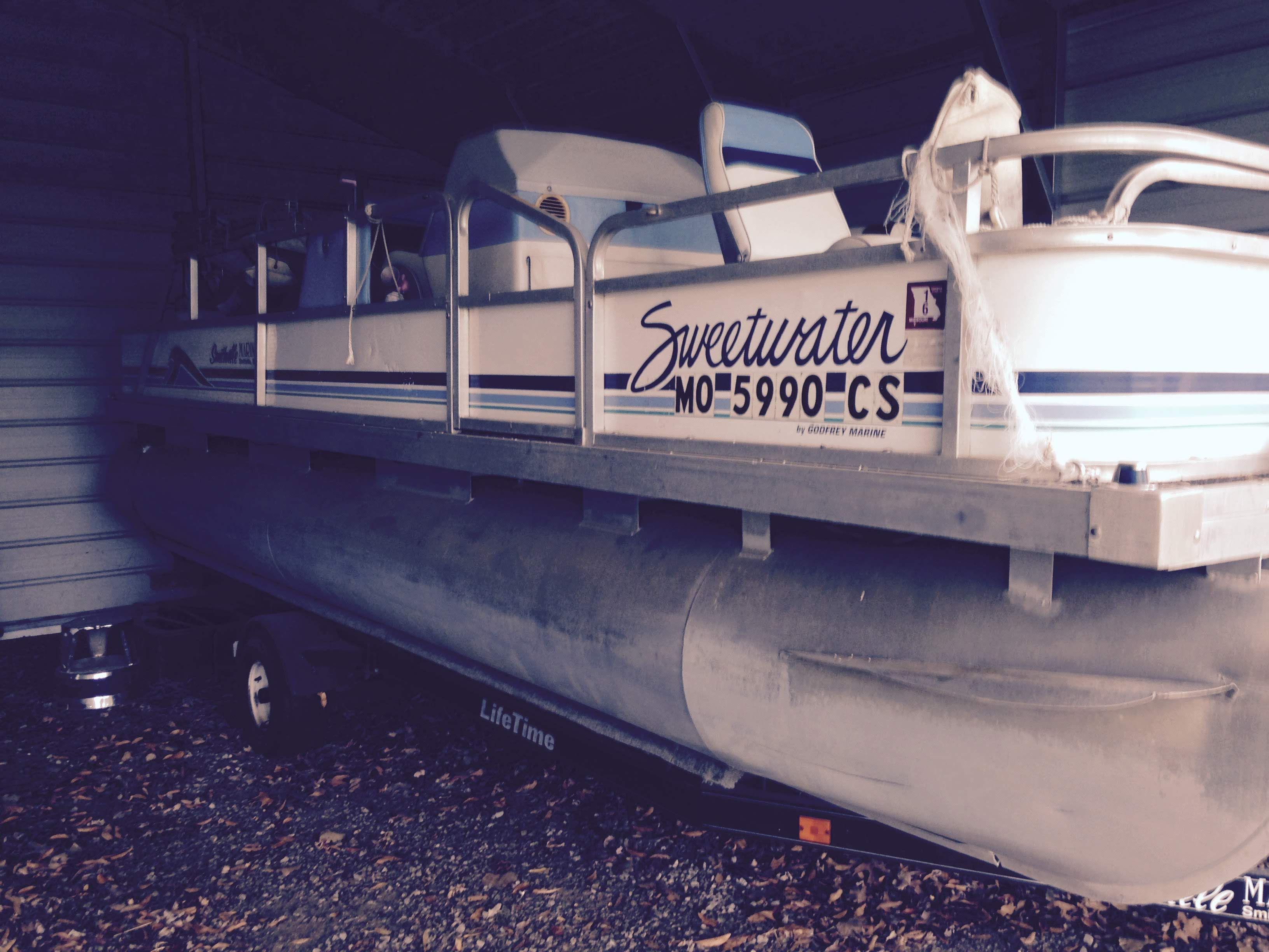 A 1993 Godfrey Sweetwater pontoon boat is parked in a shed on a trailer.