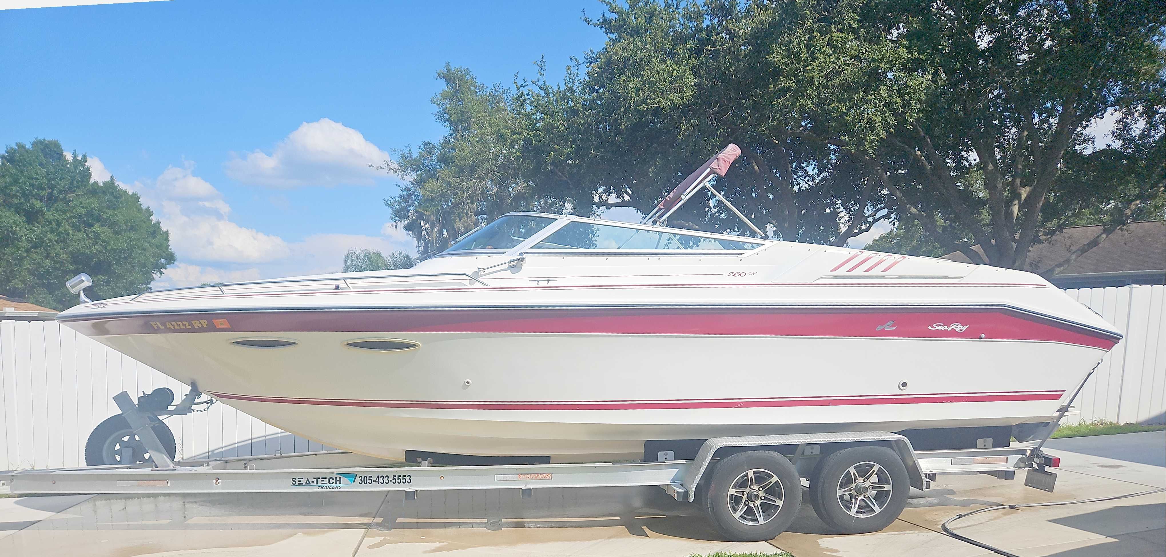 A white 1989 Sea Ray 260 Overnighter boat on a trailer in a yard.