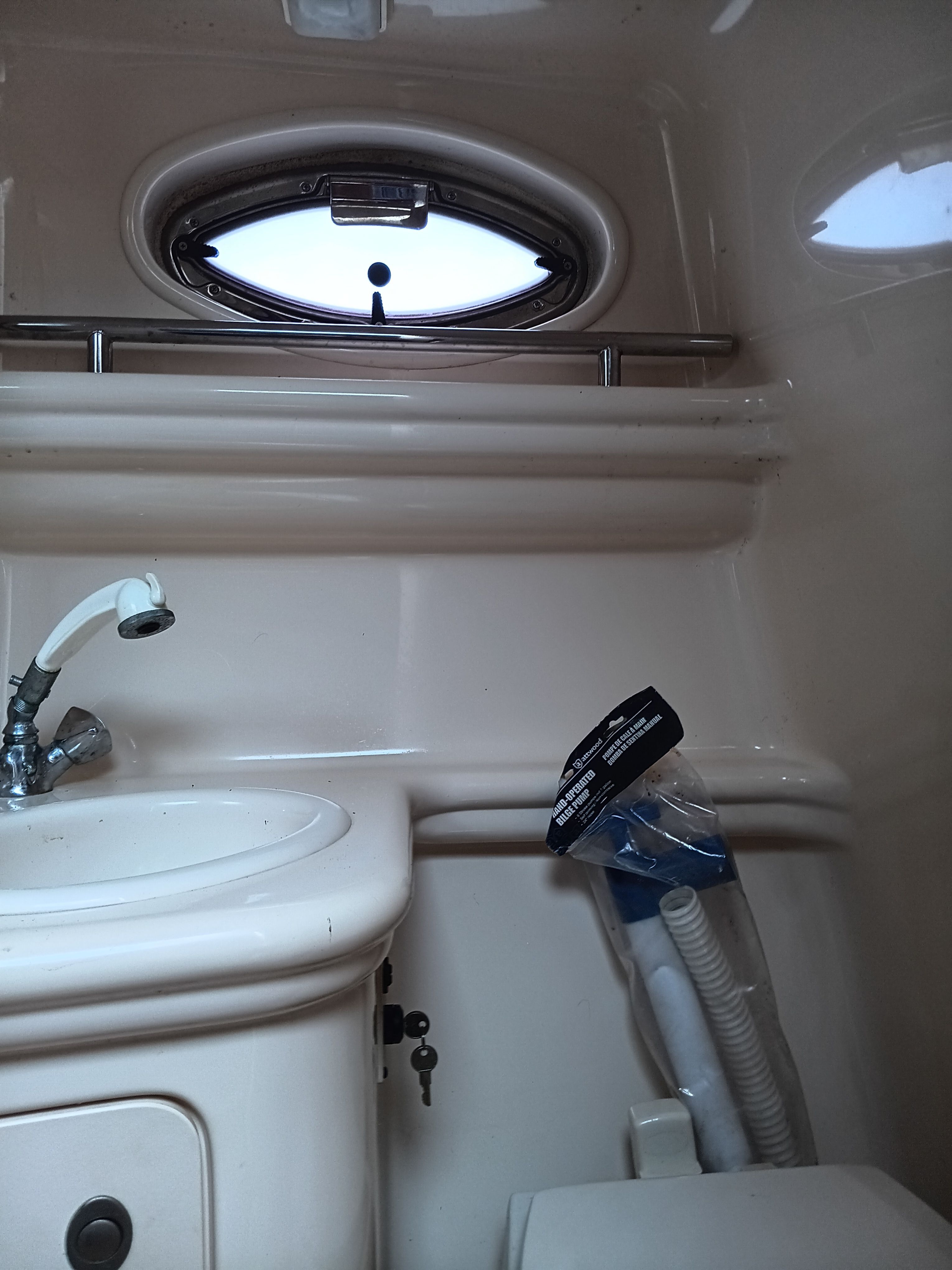 Interior view of a boat bathroom with sink, toilet, and porthole.