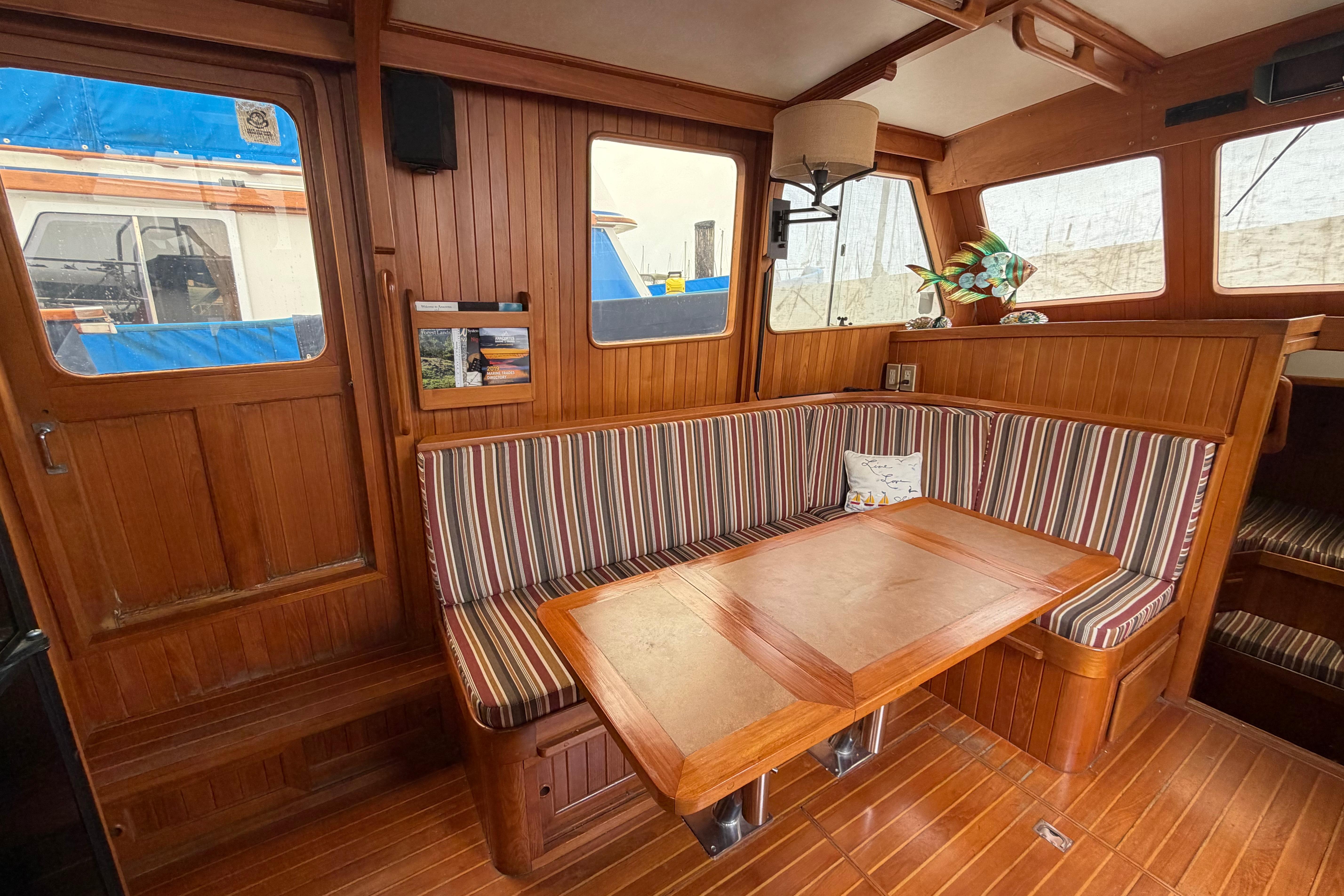 Cozy 1988 Monk 36 boat interior with striped seating and wooden table.