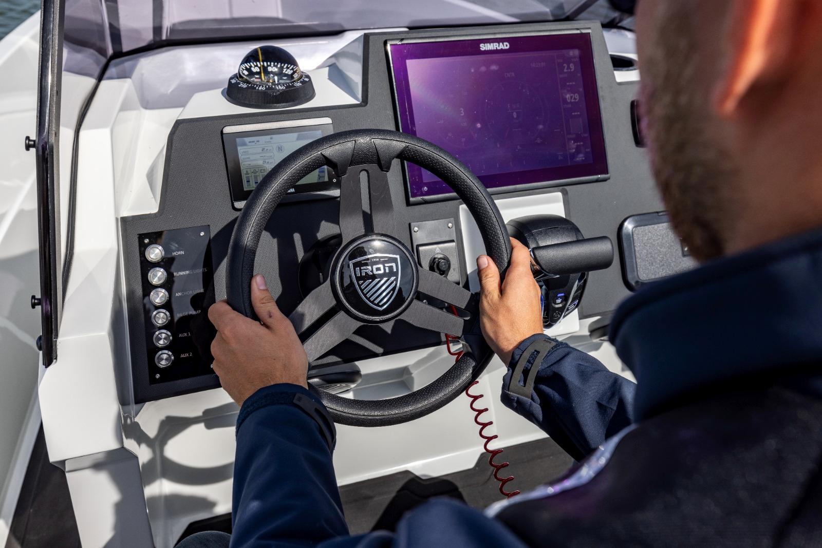 Person steering 2022 Iron 707 boat with modern dashboard and navigation system.