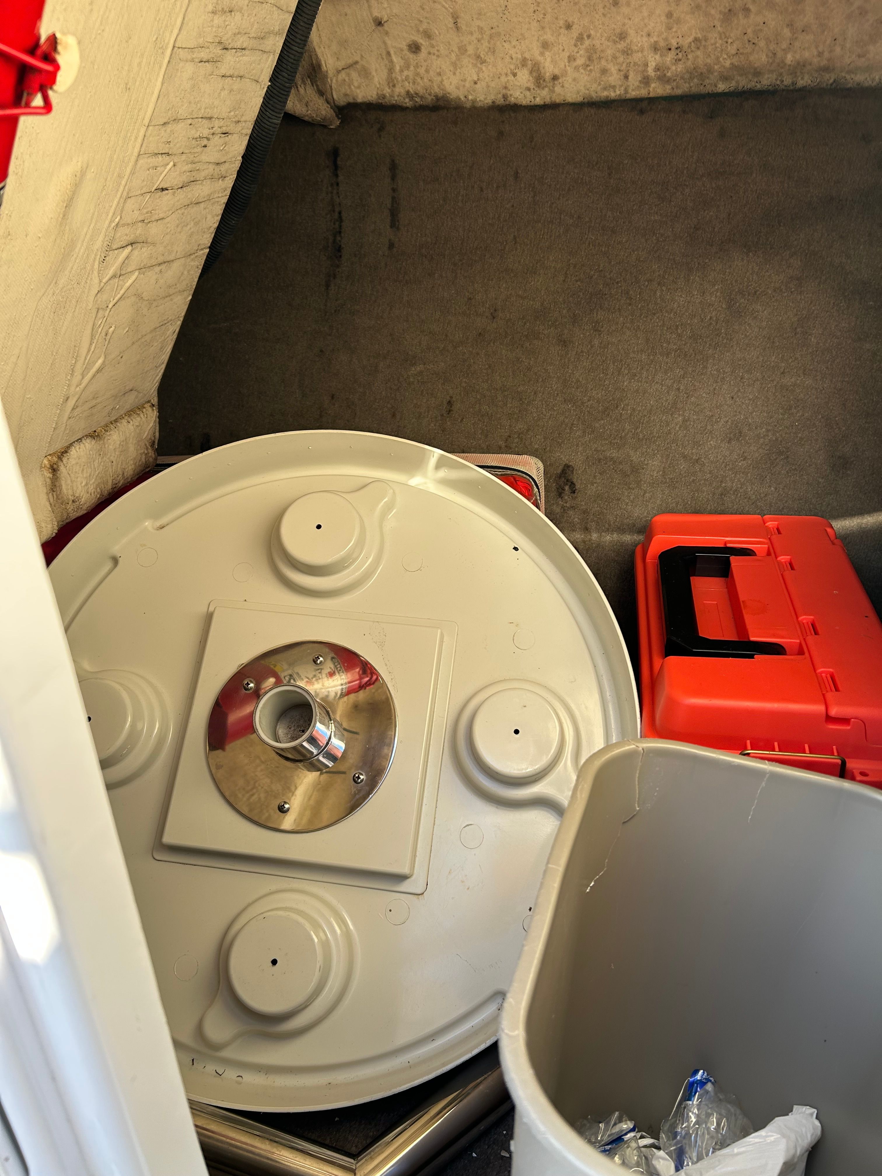 A storage area with a round table base, a red toolbox, and a gray container.