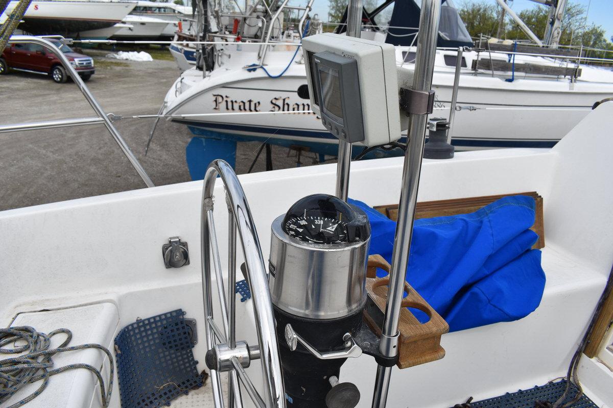The image shows a sailboat cockpit with a steering wheel and compass.