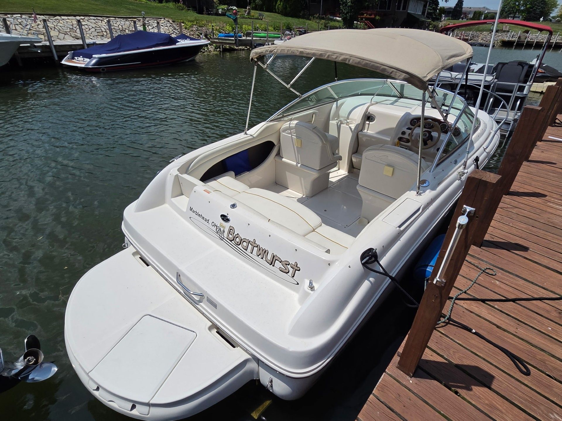 A 2002 Sea Ray 225 Weekender docked at a wooden pier. It features a beige canopy.