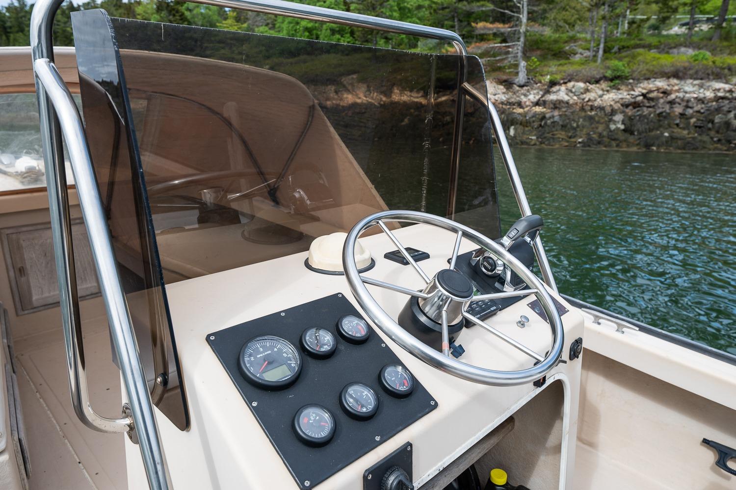 1989 Ellis 24 Open boat dashboard with steering wheel and gauges, near a scenic shoreline.