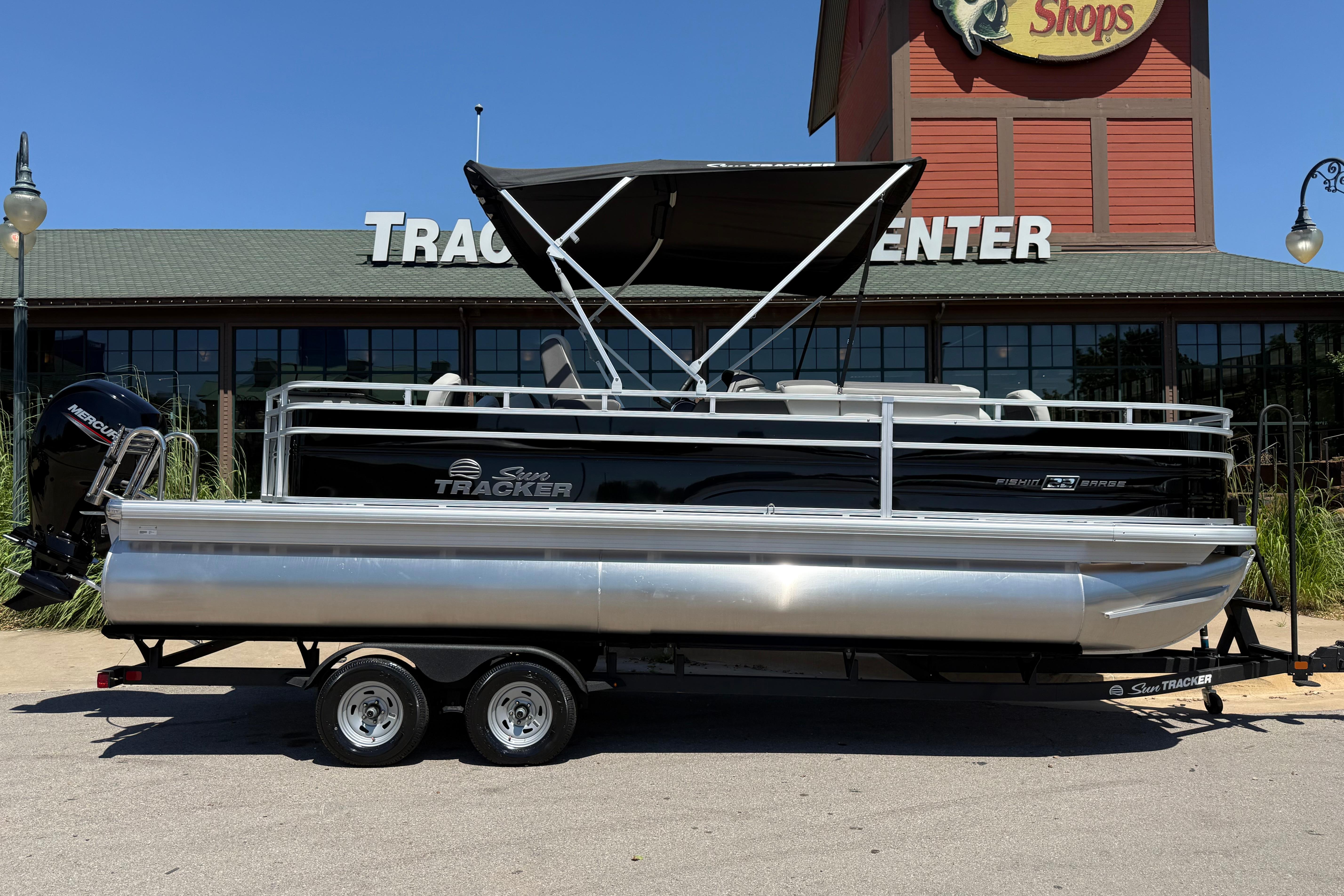 2026 Sun Tracker Fishin' Barge 22 DLX pontoon boat parked outside a store.