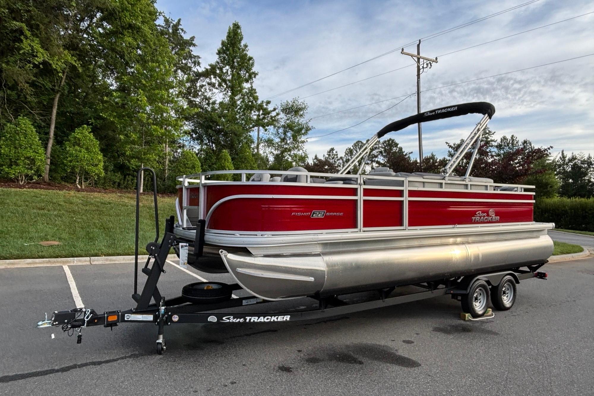 2026 Sun Tracker Fishin' Barge 22 DLX pontoon boat on trailer in parking lot.