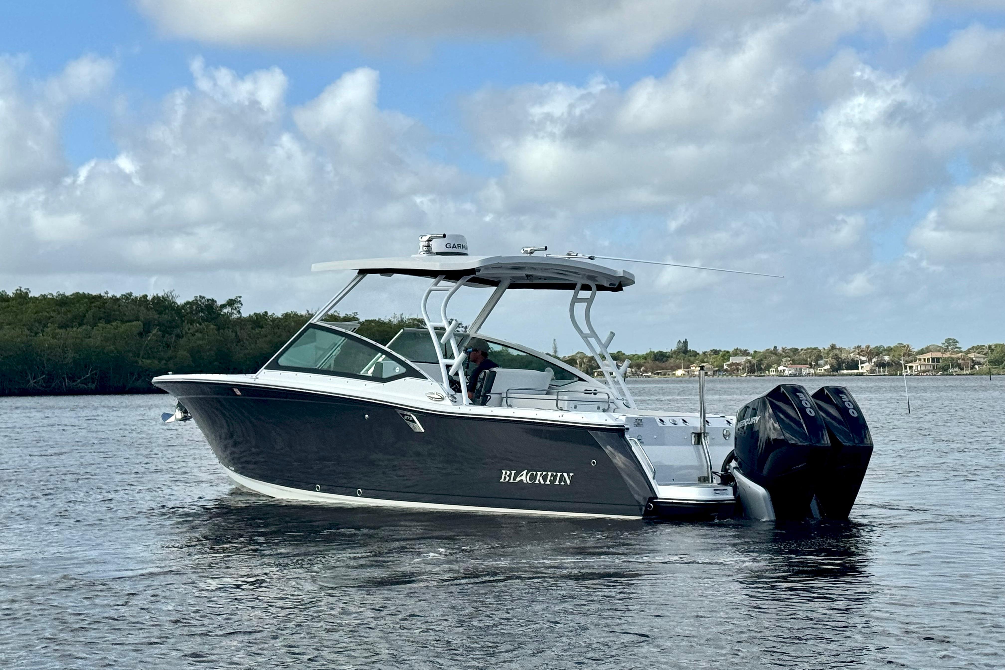 2023 Blackfin 272 DC boat cruising on a calm waterway under a cloudy sky.