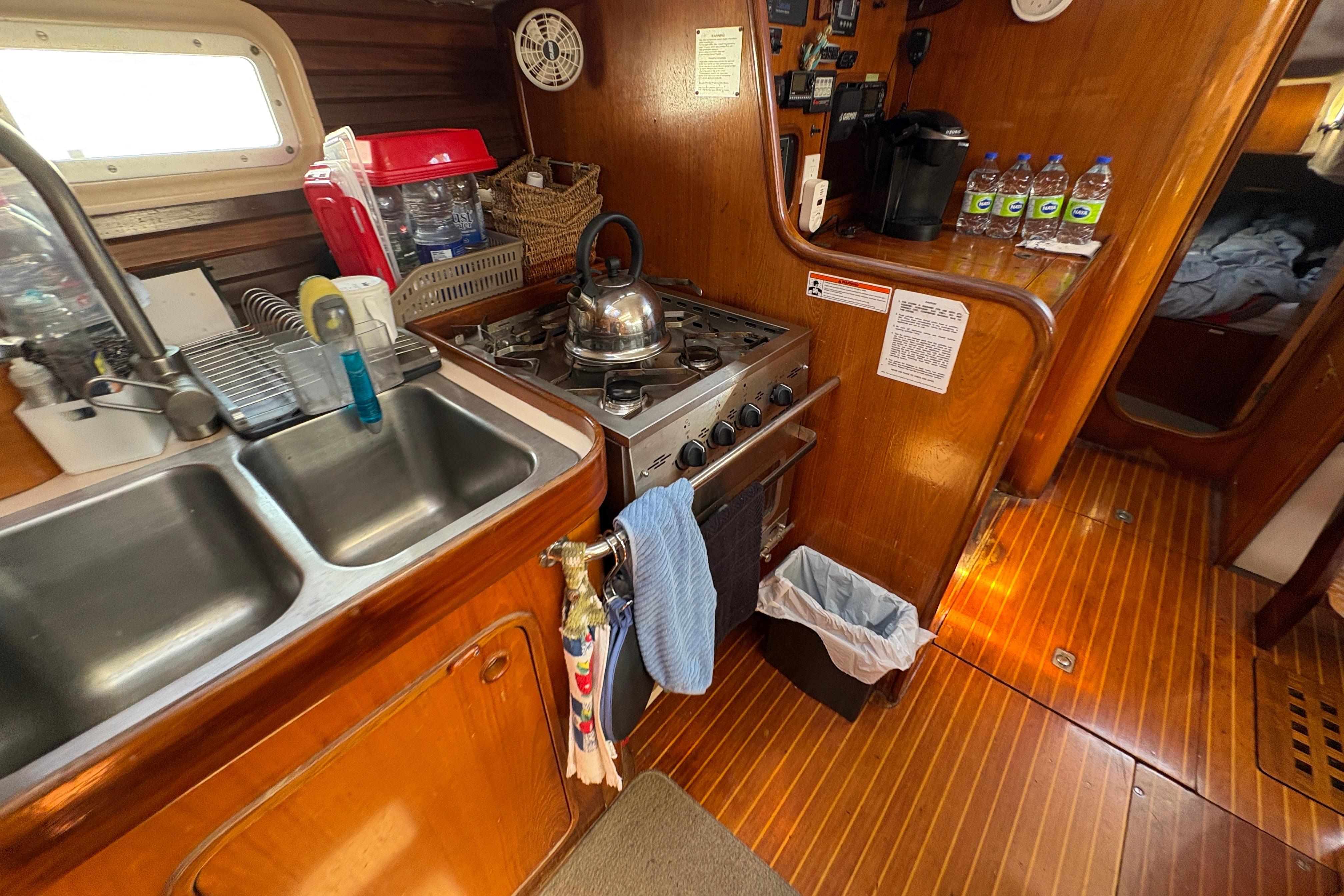Galley kitchen in 1990 Beneteau Oceanis 500 sailboat with stove, sink, and wooden cabinetry.