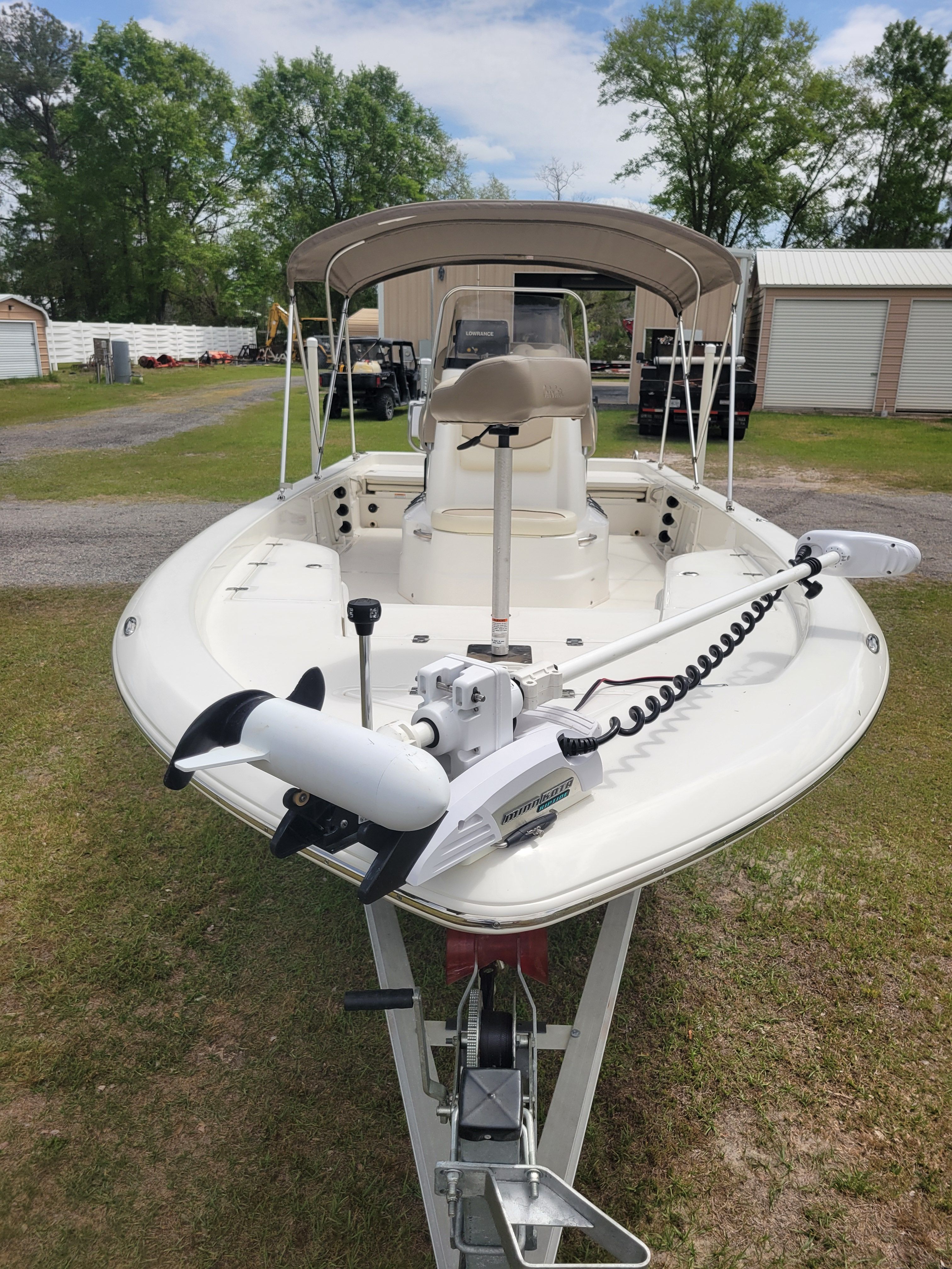 A white boat with a sunshade is on a trailer on a grassy area.