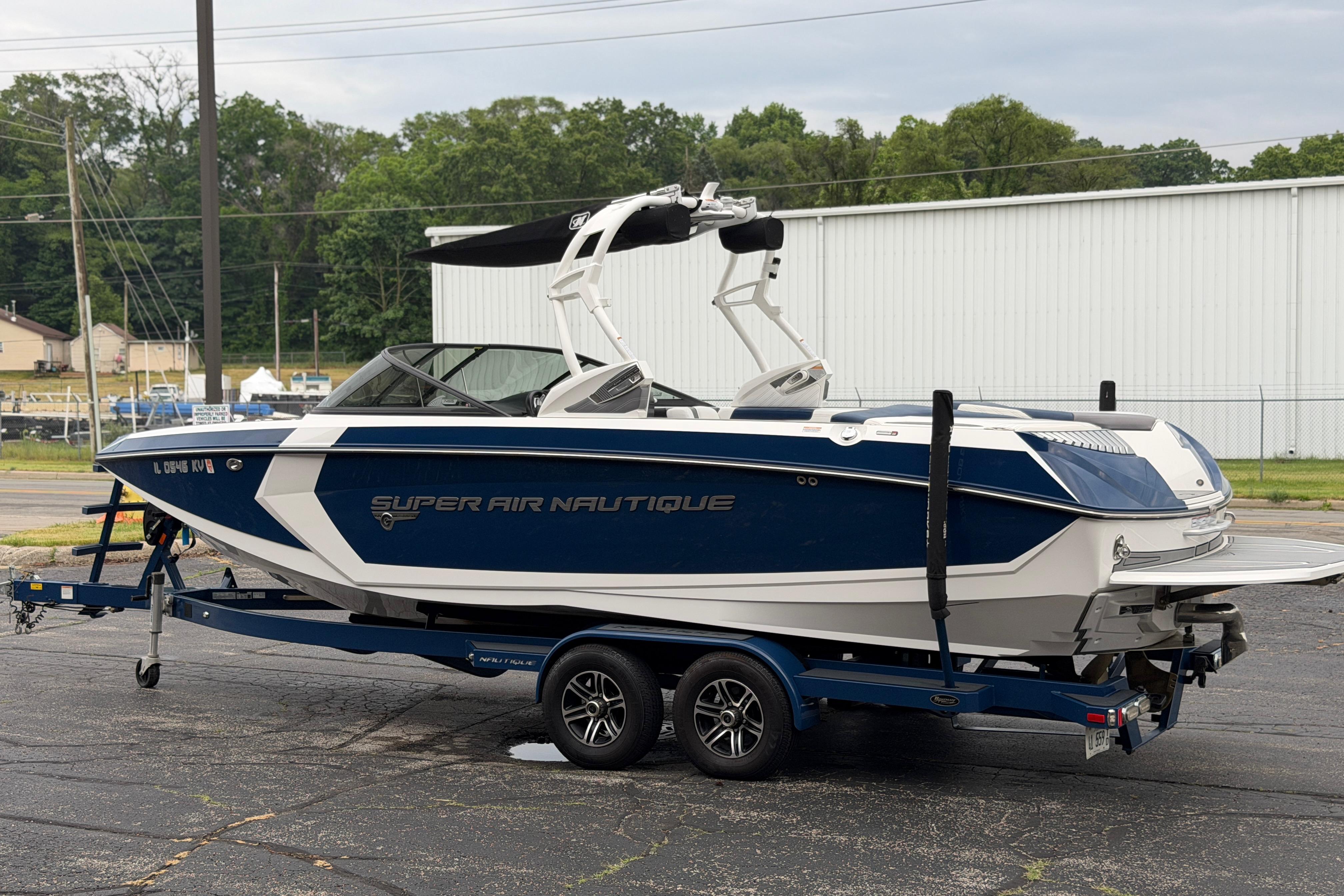 2016 Naitique G25 boat on trailer, blue and white design, parked outdoors.