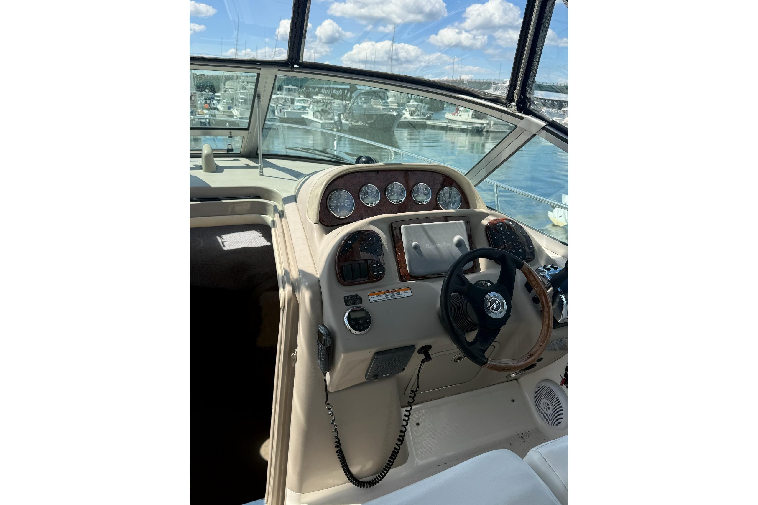 Helm of 2006 Sea Ray 300 Sundancer with steering wheel and gauges, docked at marina.