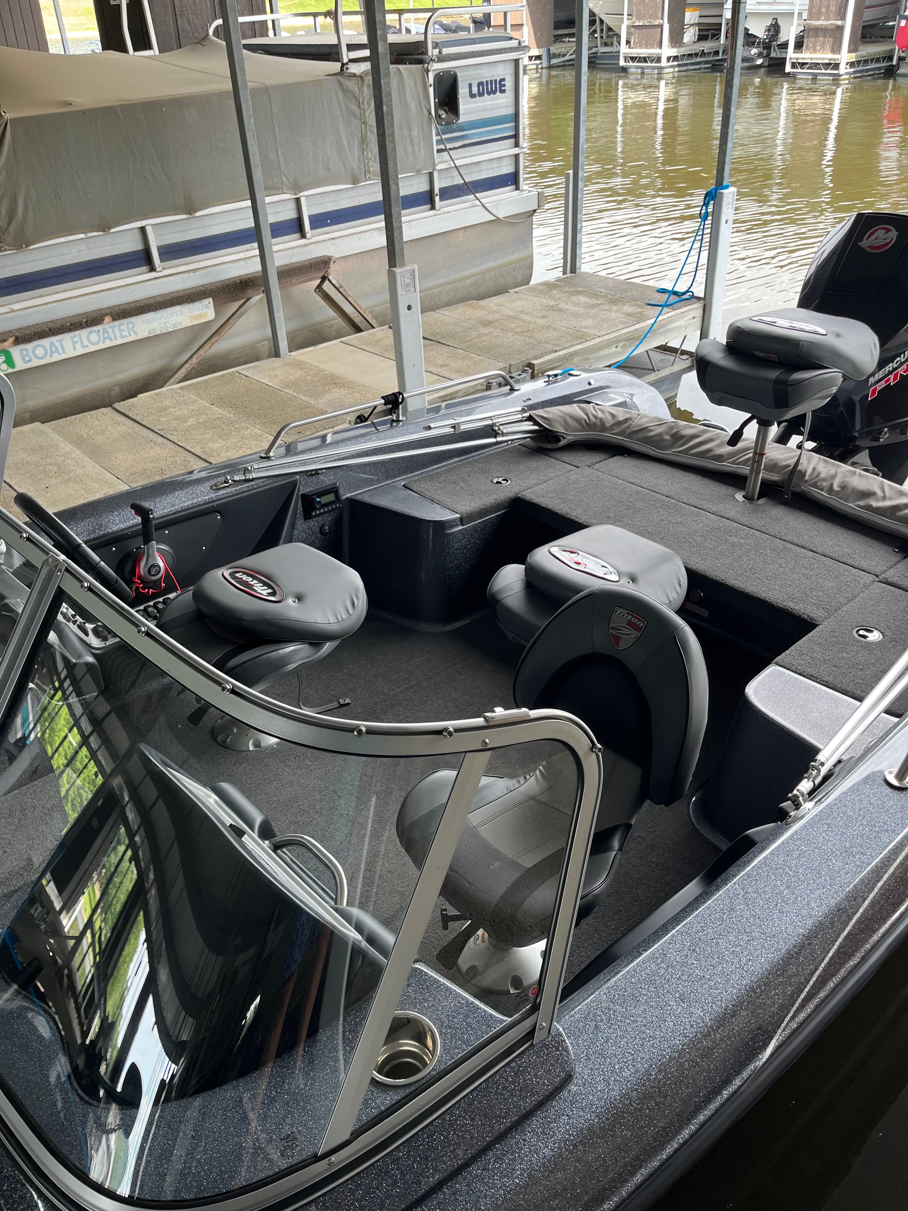 The image shows a modern fishing boat with gray seats and a clear windshield. It is docked.