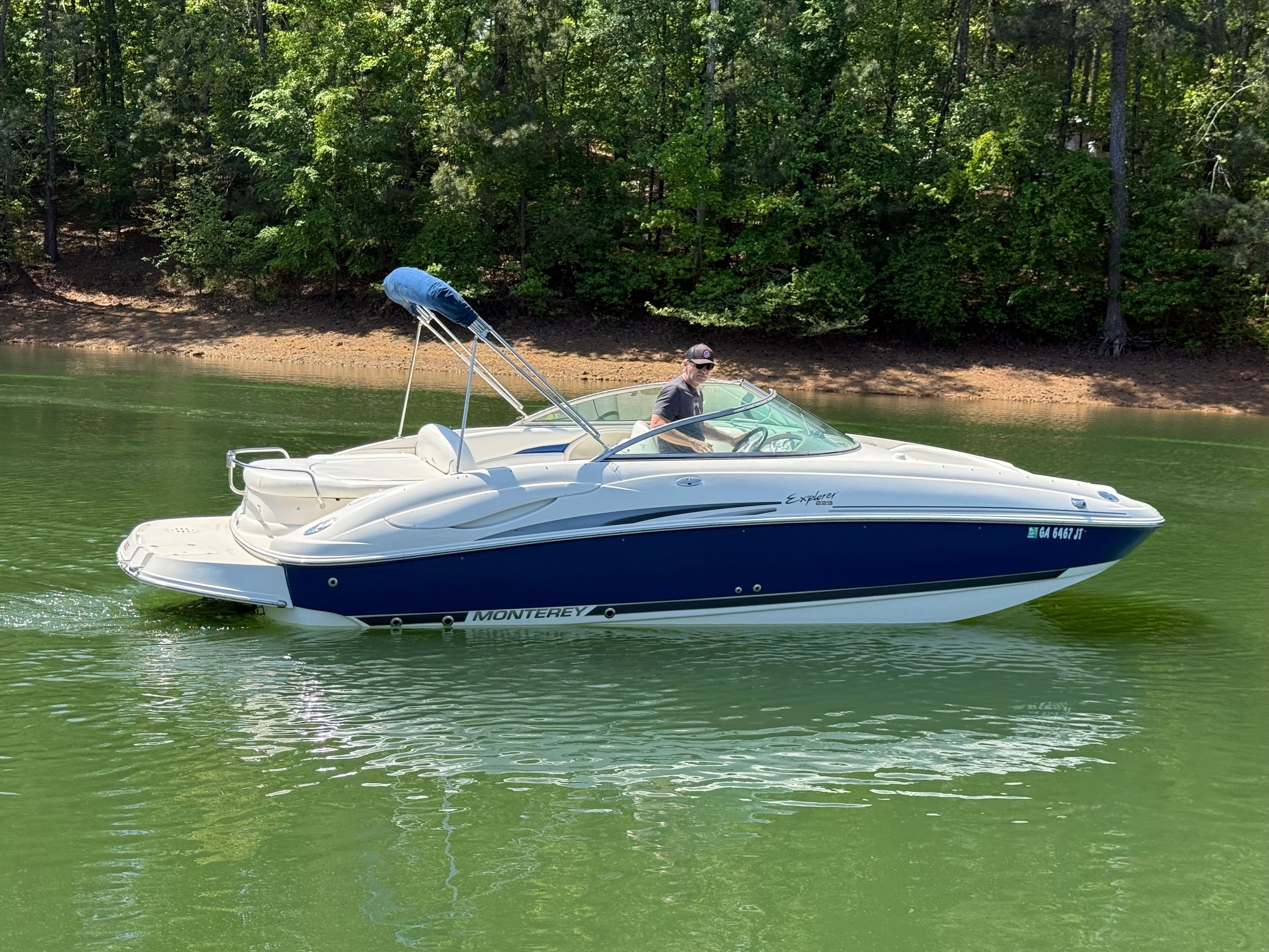 A white and blue 2005 Monterey 223 Explorer Sport boat cruising on a calm lake.