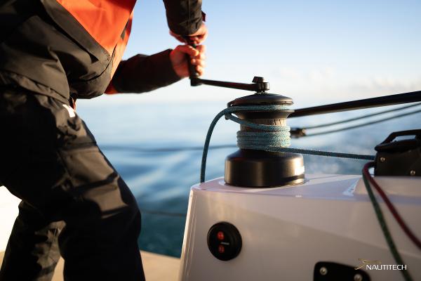 Person operating winch on 2025 Nautitech 48 Open catamaran, sailing on calm waters.