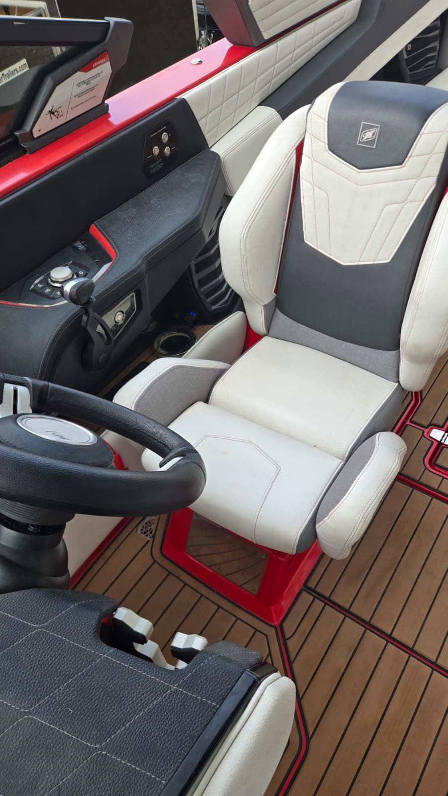 A modern boat cockpit with a white and gray seat, steering wheel, and control console.