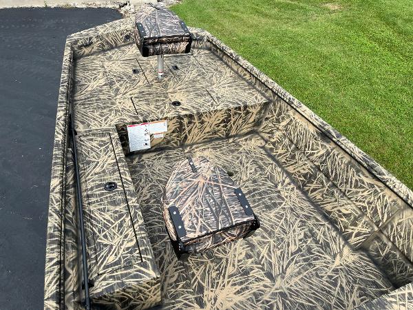 2024 Lowe Roughneck 1660 boat with camouflage interior, parked on driveway next to grass.