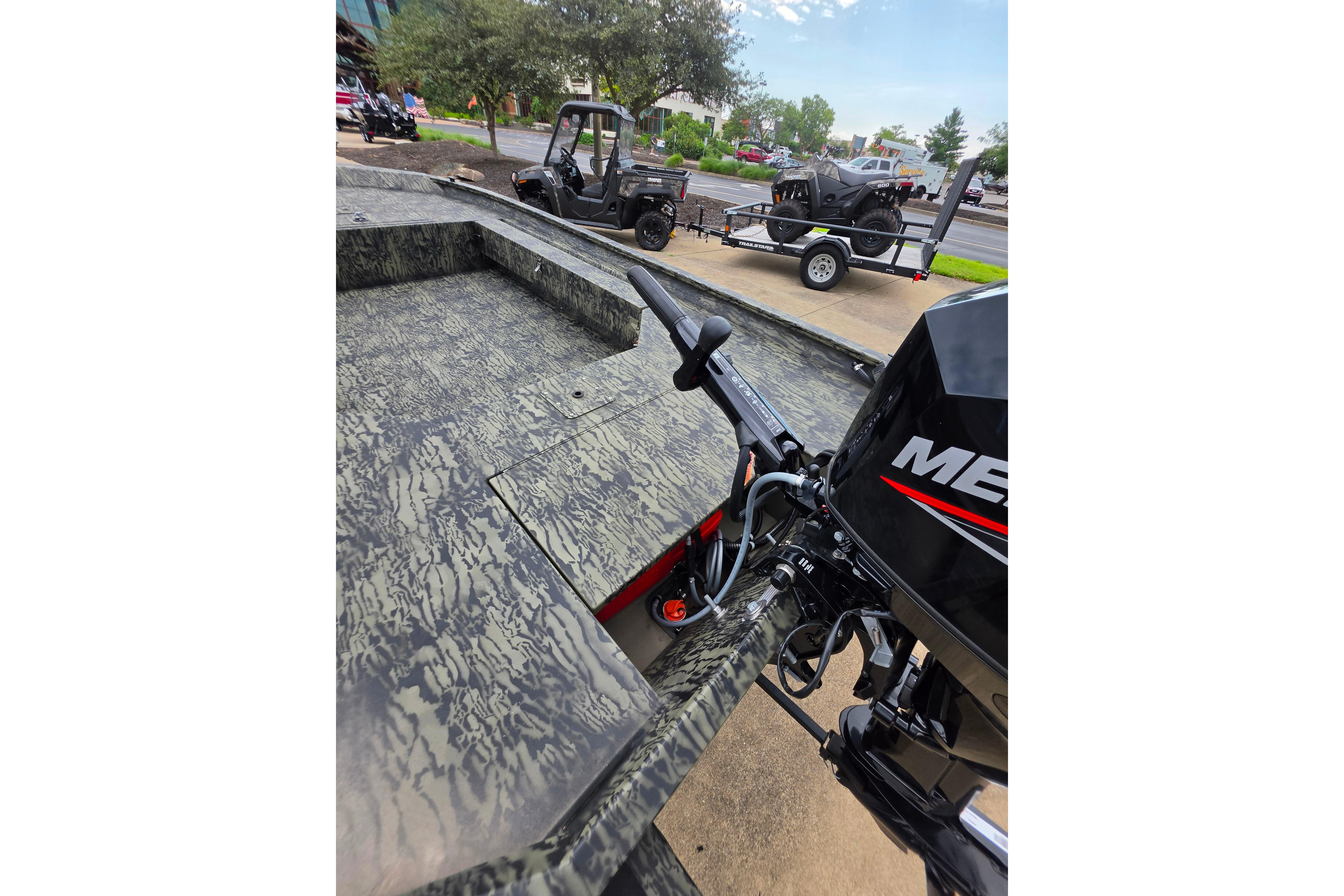 2026 Tracker Grizzly 1654 T Sportsman boat with Mercury engine, parked near ATV on trailer.