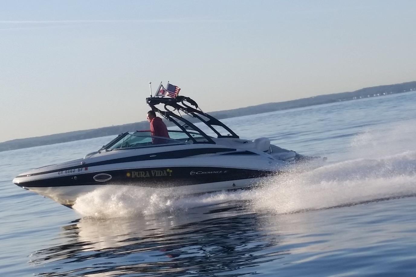 2013 Crownline Eclipse E4 speedboat cruising on a calm lake with flags waving.