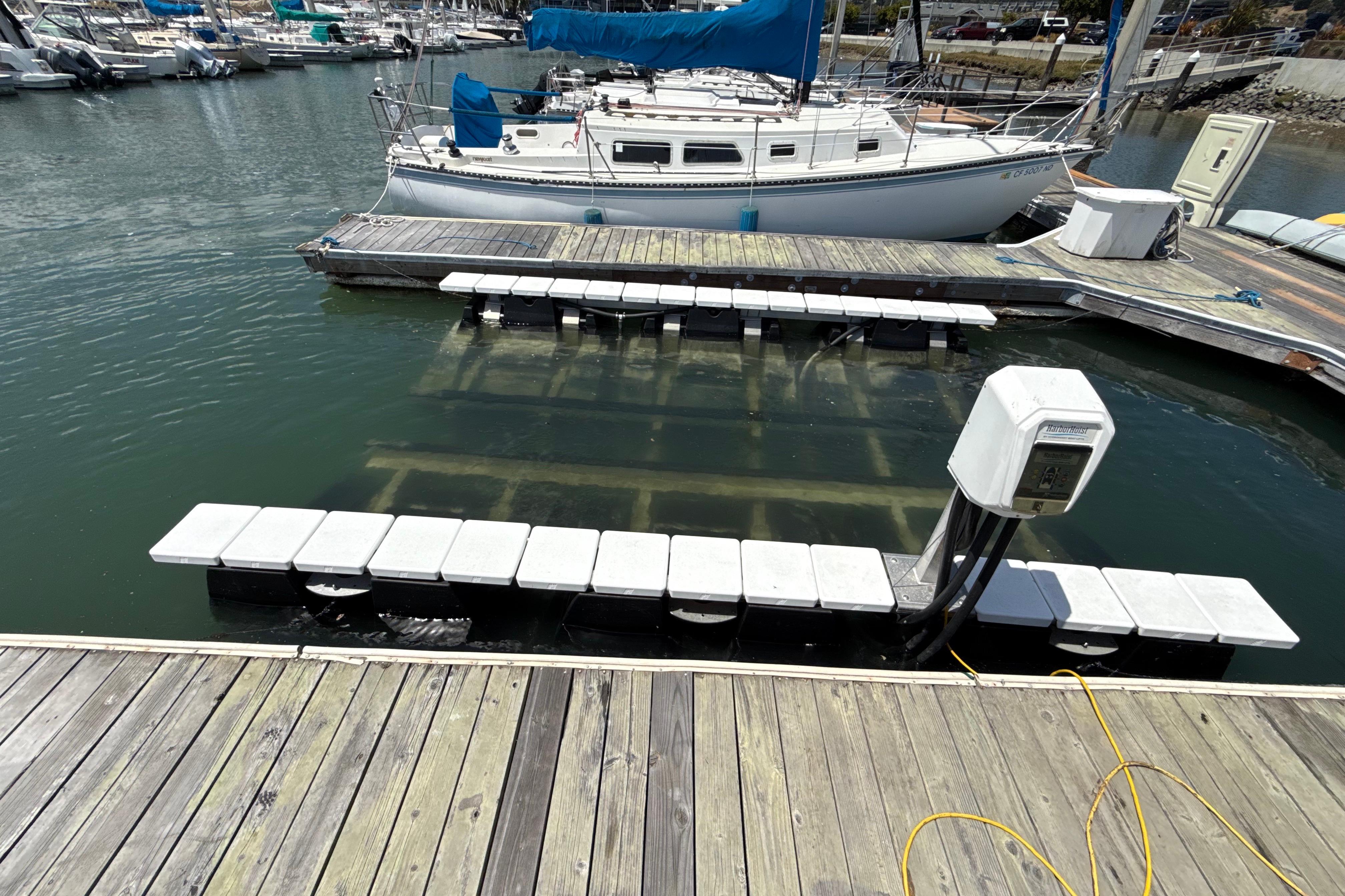 Docked sailboat near a marina with floating platforms and electrical hookup.