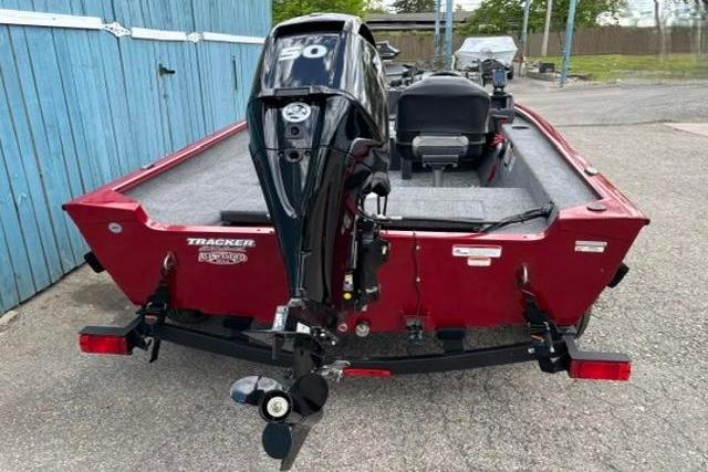 Red 2025 Tracker Super Guide V-16 SC boat with outboard motor, parked near blue fence.